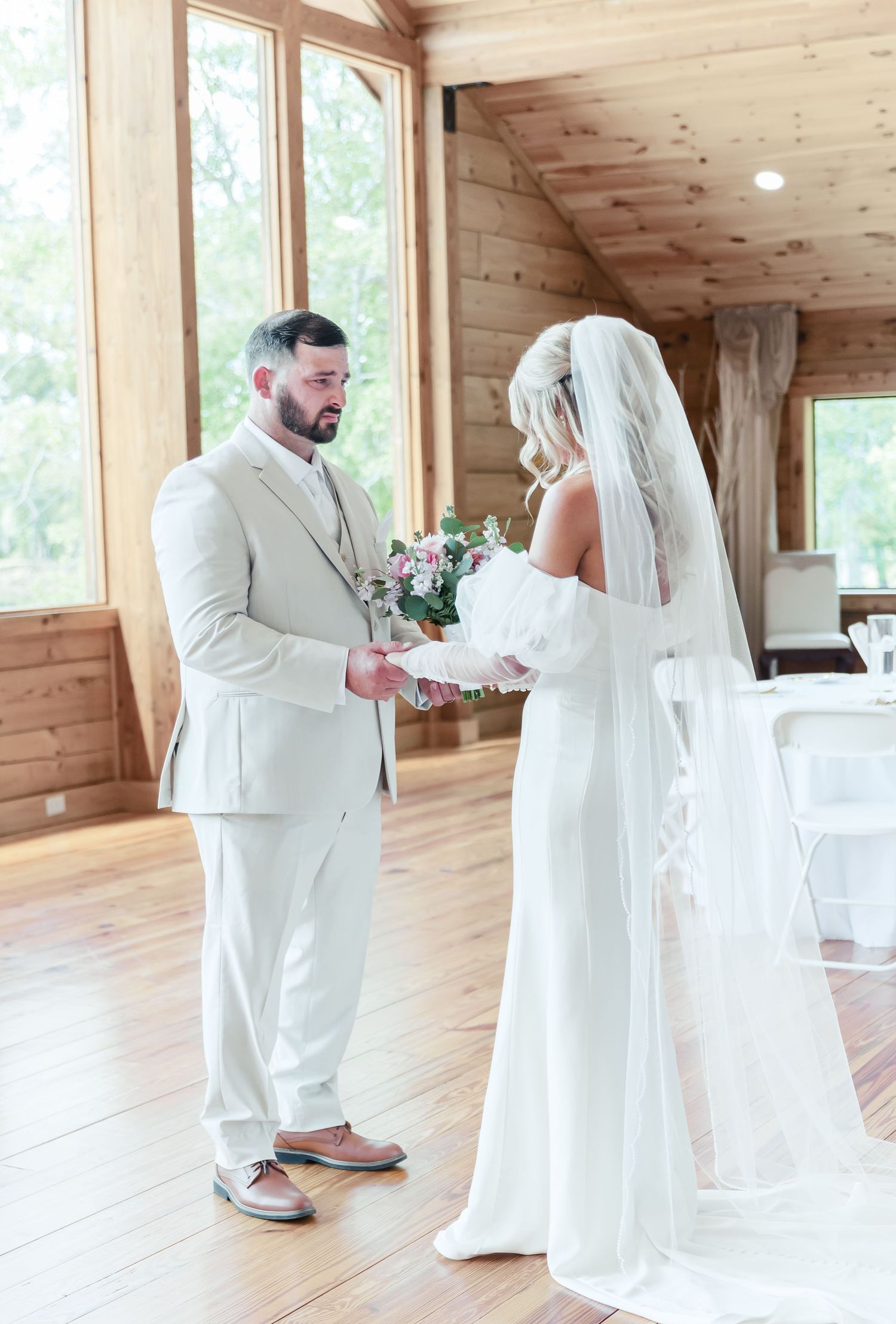 Couple exchanges flowers during their wedding ceremony in a sunlit wooden venue.