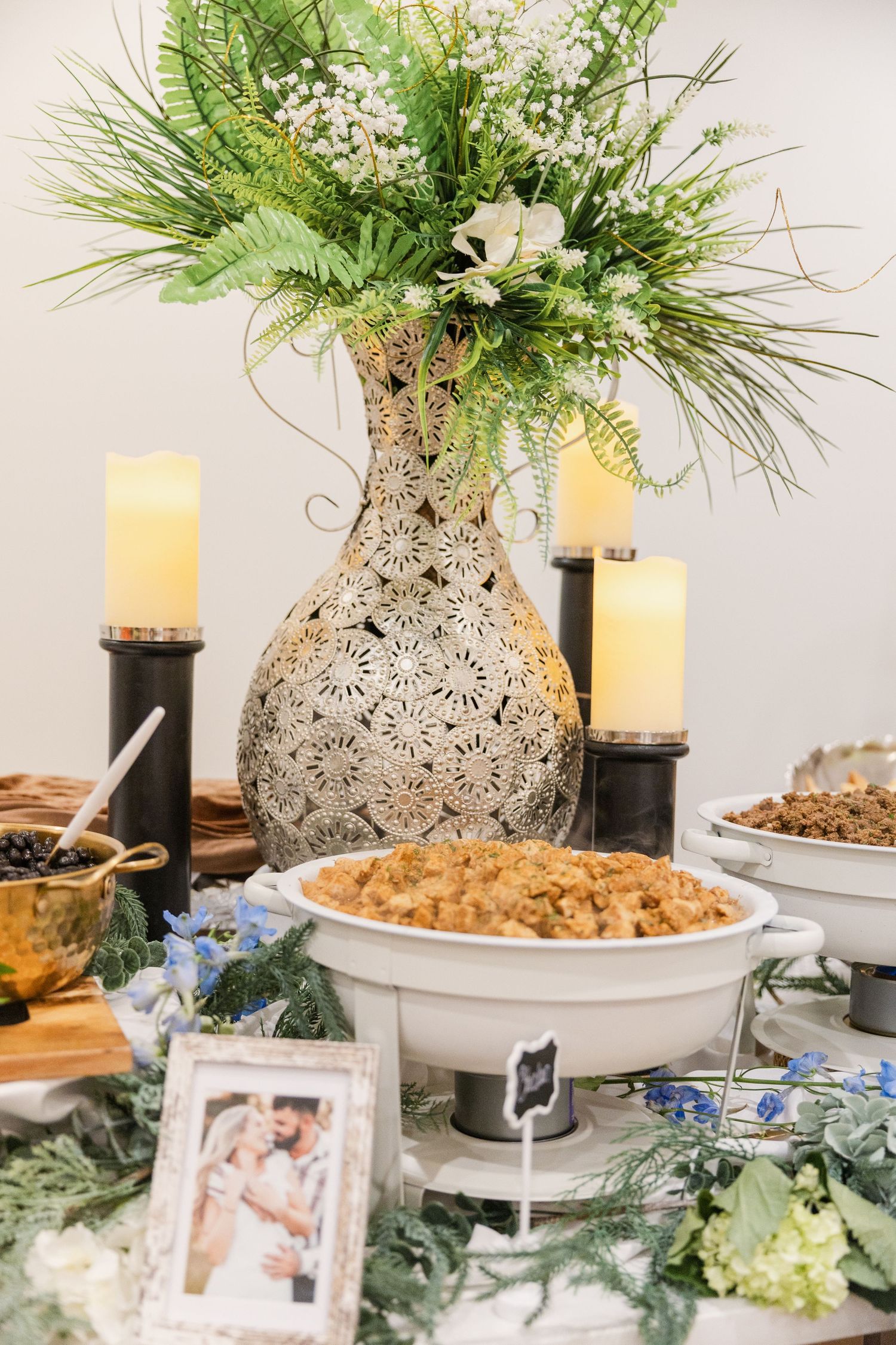 Elegant wedding reception buffet table with decorative vase centerpiece, candles, and floral greenery.