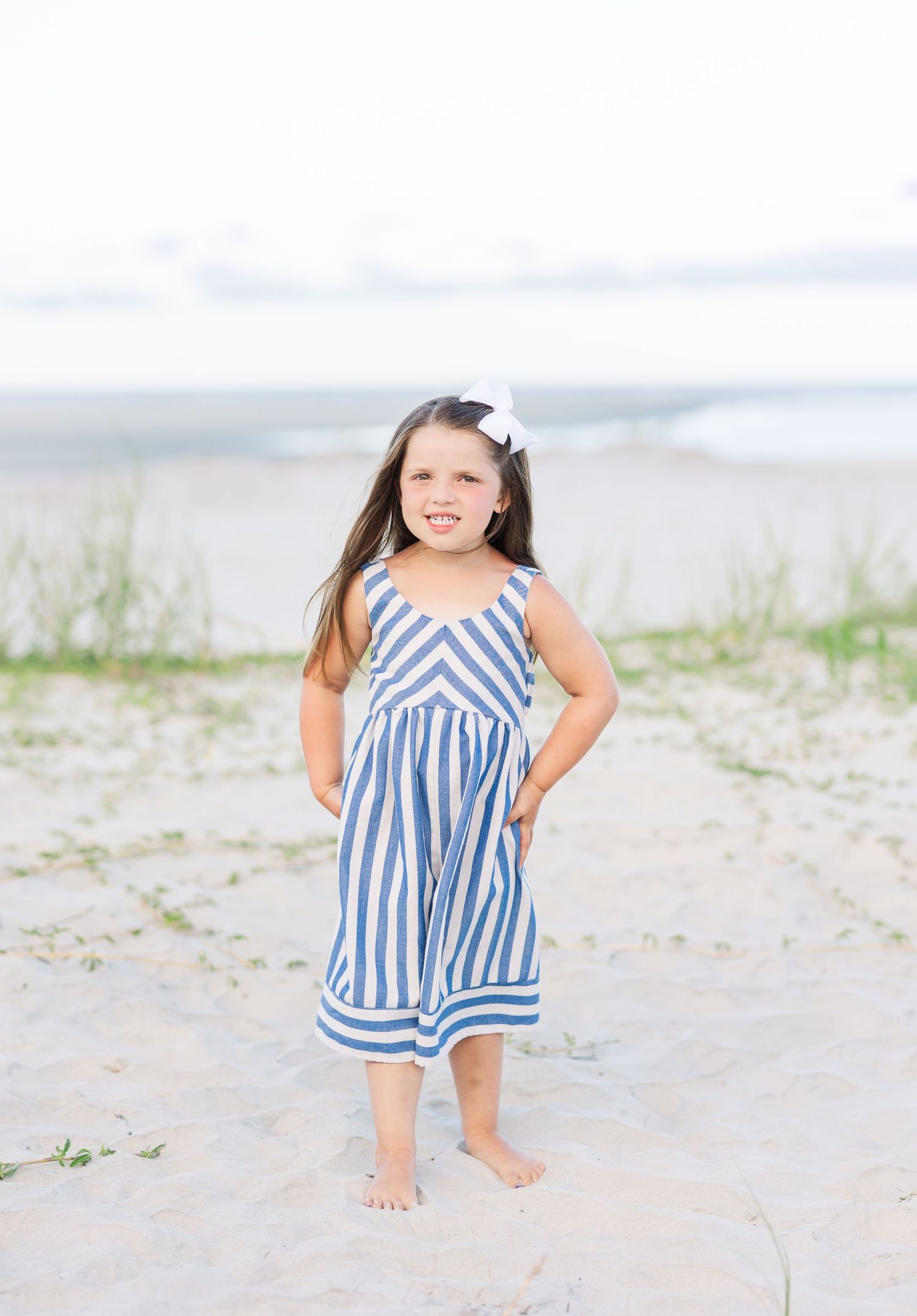A striped blue and white sundress being worn on a sunny beach with sand dunes in the background.