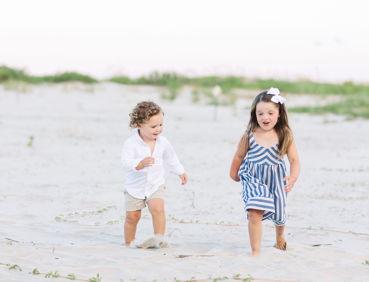Children playing and running in the sand at the beach on a sunny day.