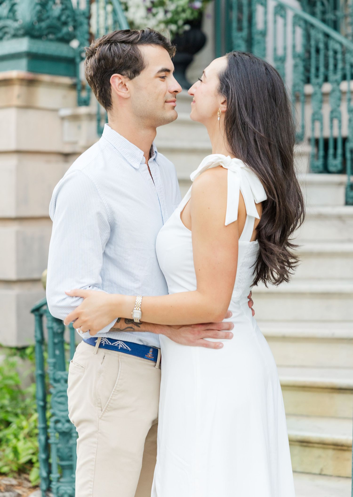 Couple gazing into each other's eyes near ornate green ironwork, man in white shirt and khakis, woman in white dress.