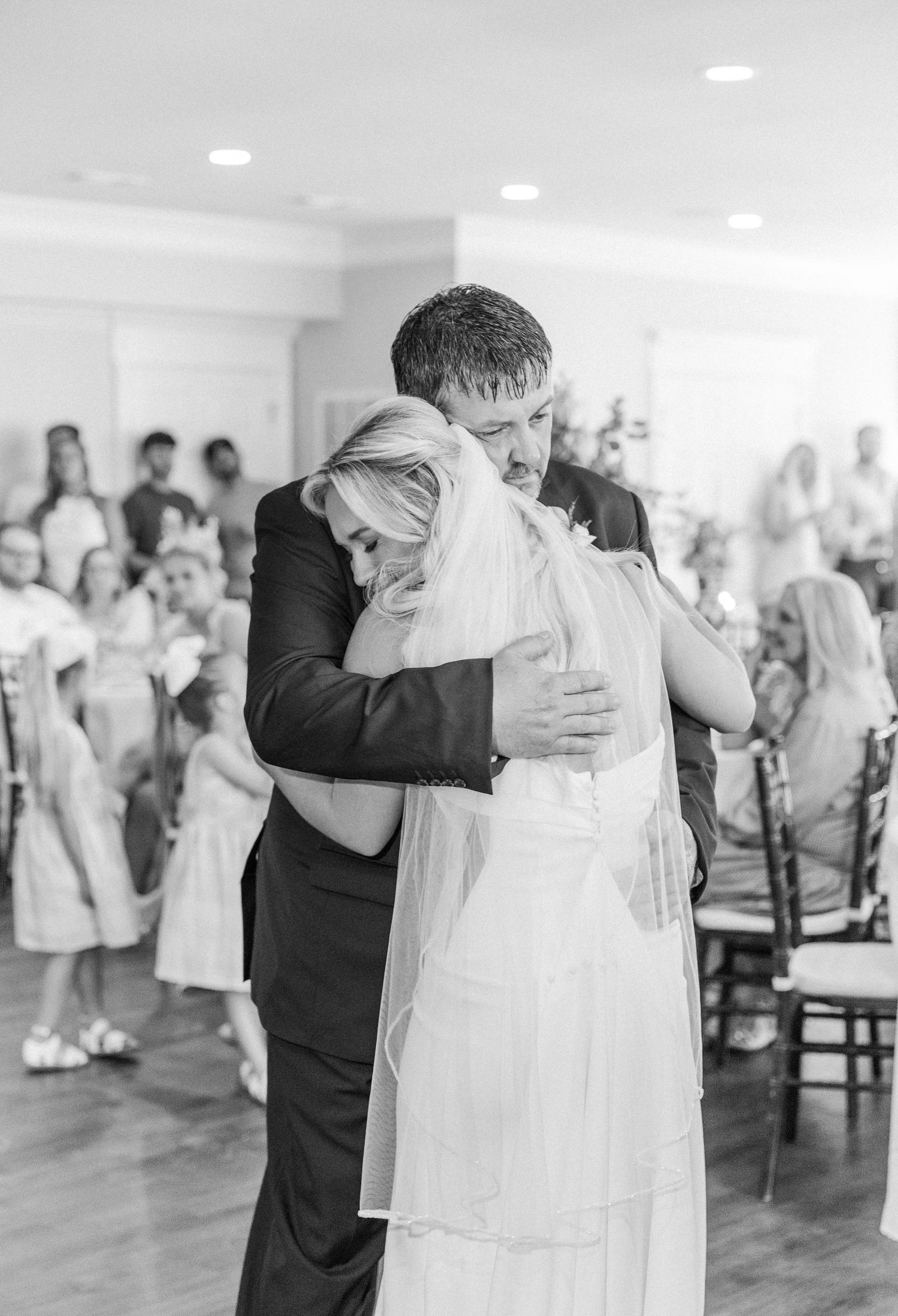 Emotional black and white photo of bride and father sharing heartfelt hug on dance floor.