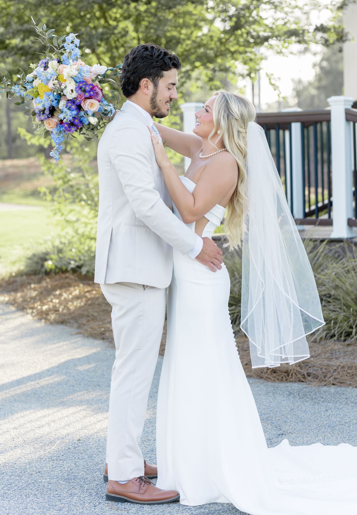 Bride and groom share a romantic moment in a garden, she in a white gown with veil, he in a beige suit.