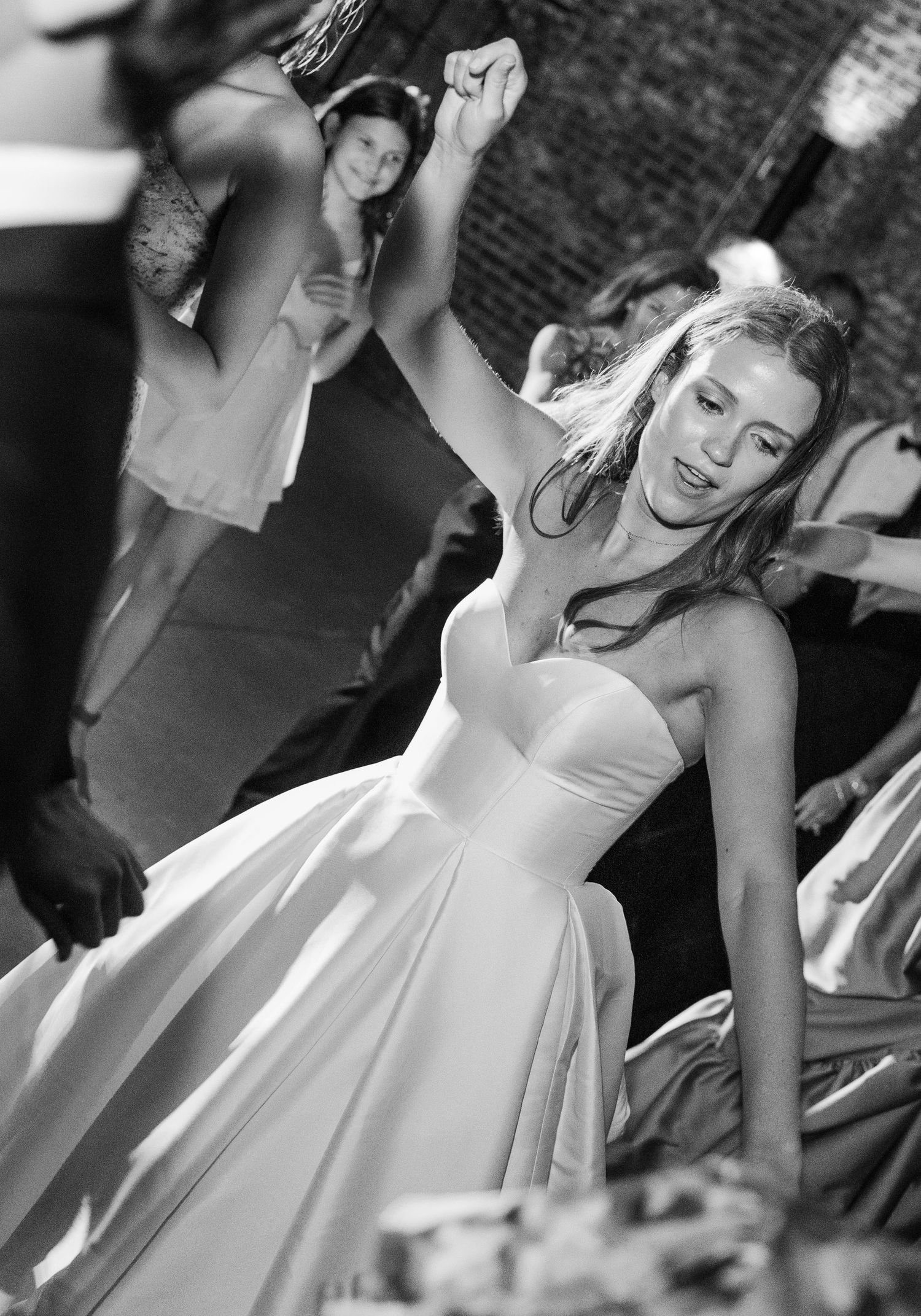 Black and white photo of bride in strapless gown dancing joyfully at wedding reception.