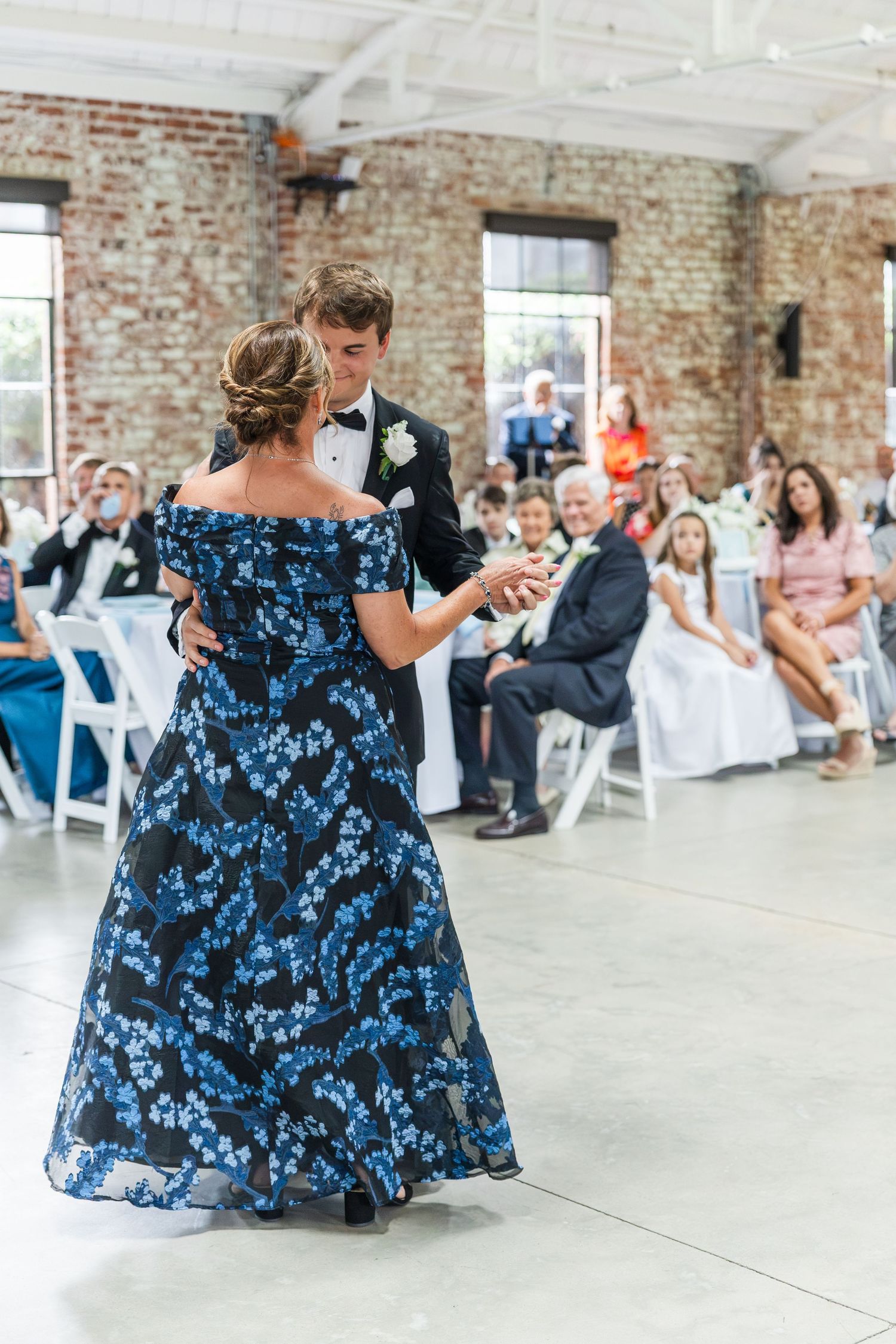 Groom shares mother-son dance in elegant brick venue while wedding guests watch and celebrate.
