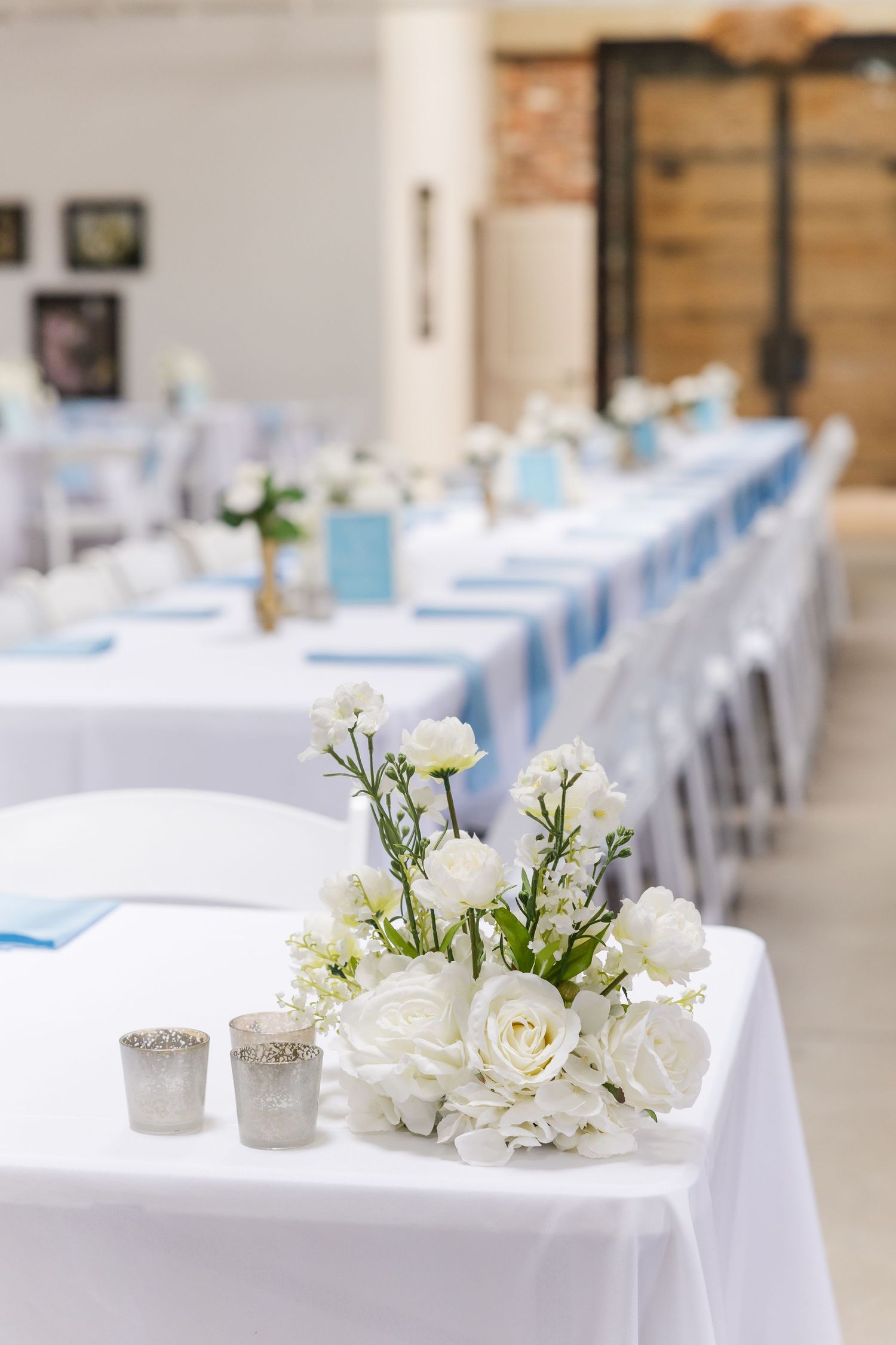 Elegant wedding reception tables with white linens, blue accents, and white floral centerpieces.
