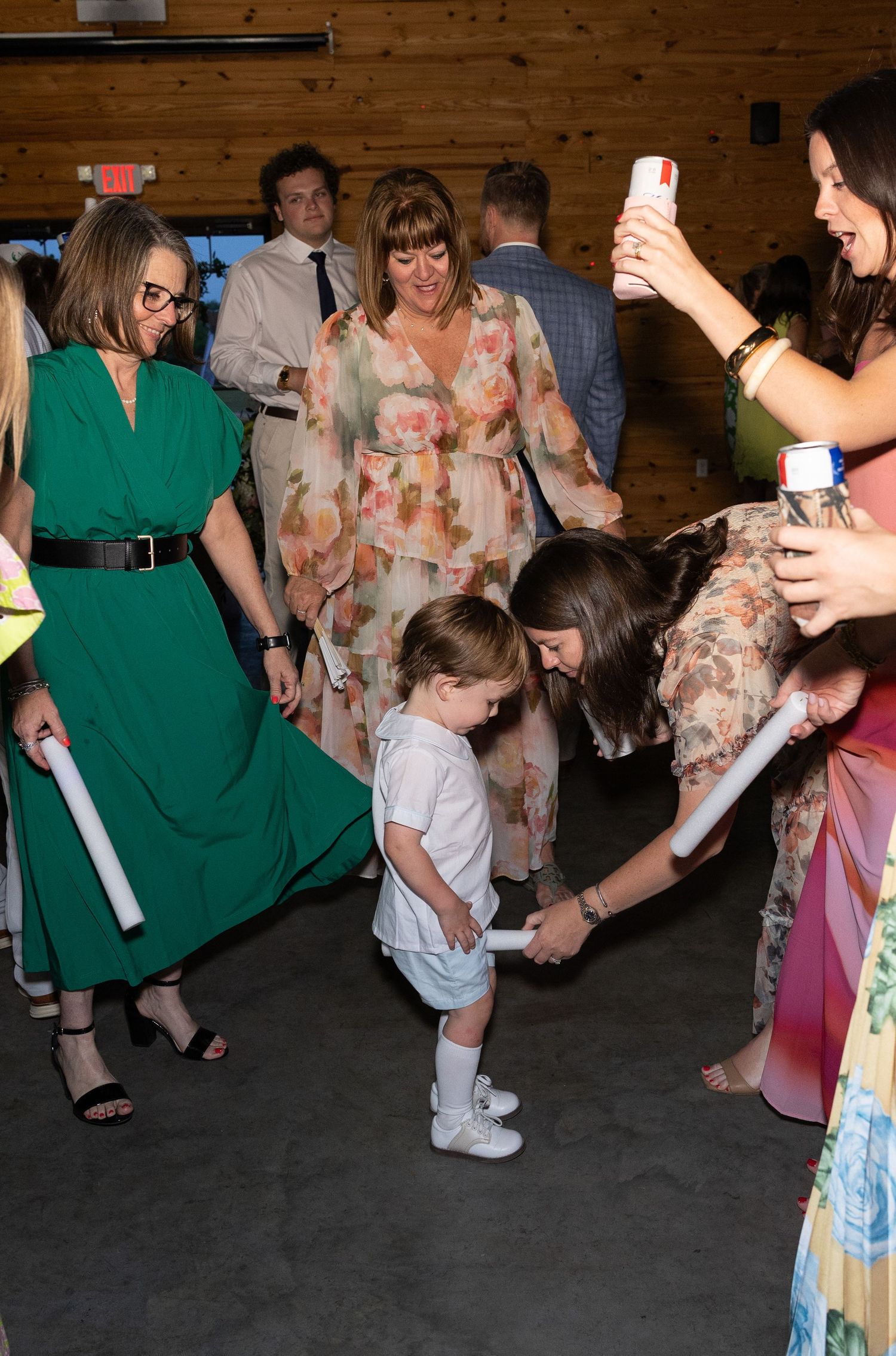 Wedding guests dancing with toddler on reception dance floor inside rustic barn venue.