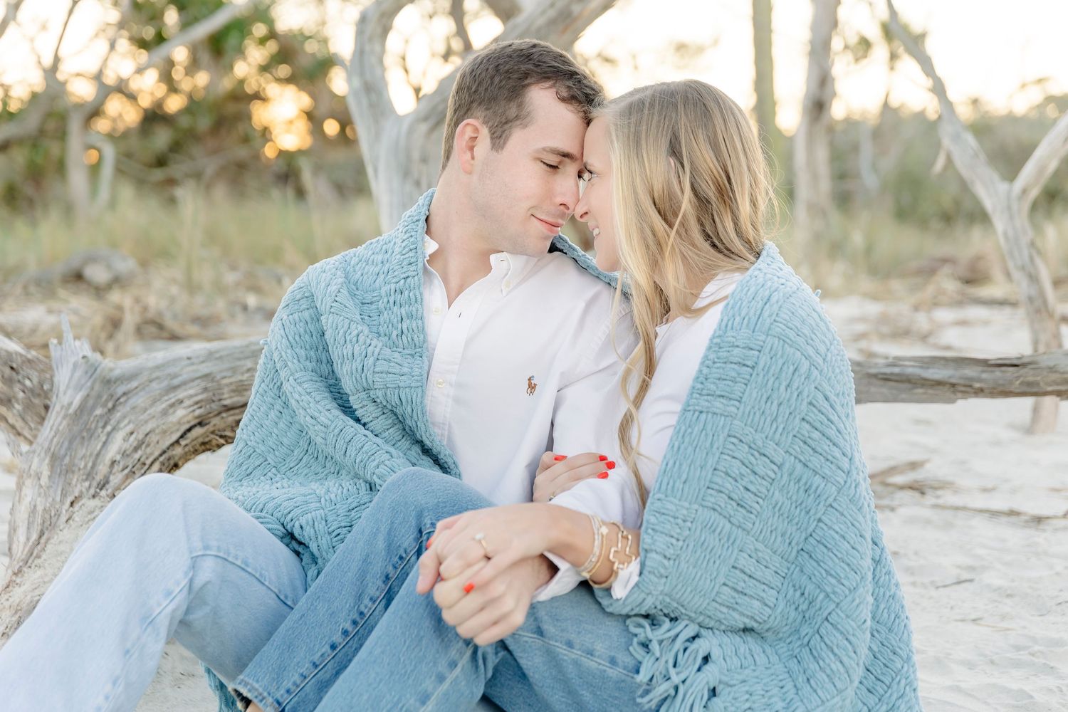 Intimate moment between couple wrapped in a blue knit sweater on a beach with driftwood.