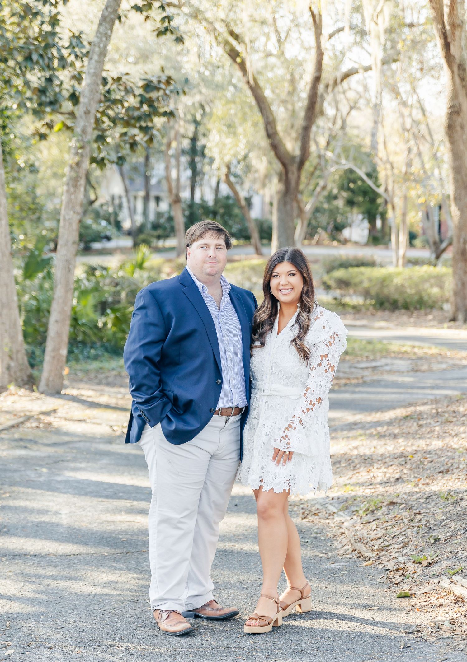 A couple poses together outdoors, wearing blue and white formal attire in a natural setting.