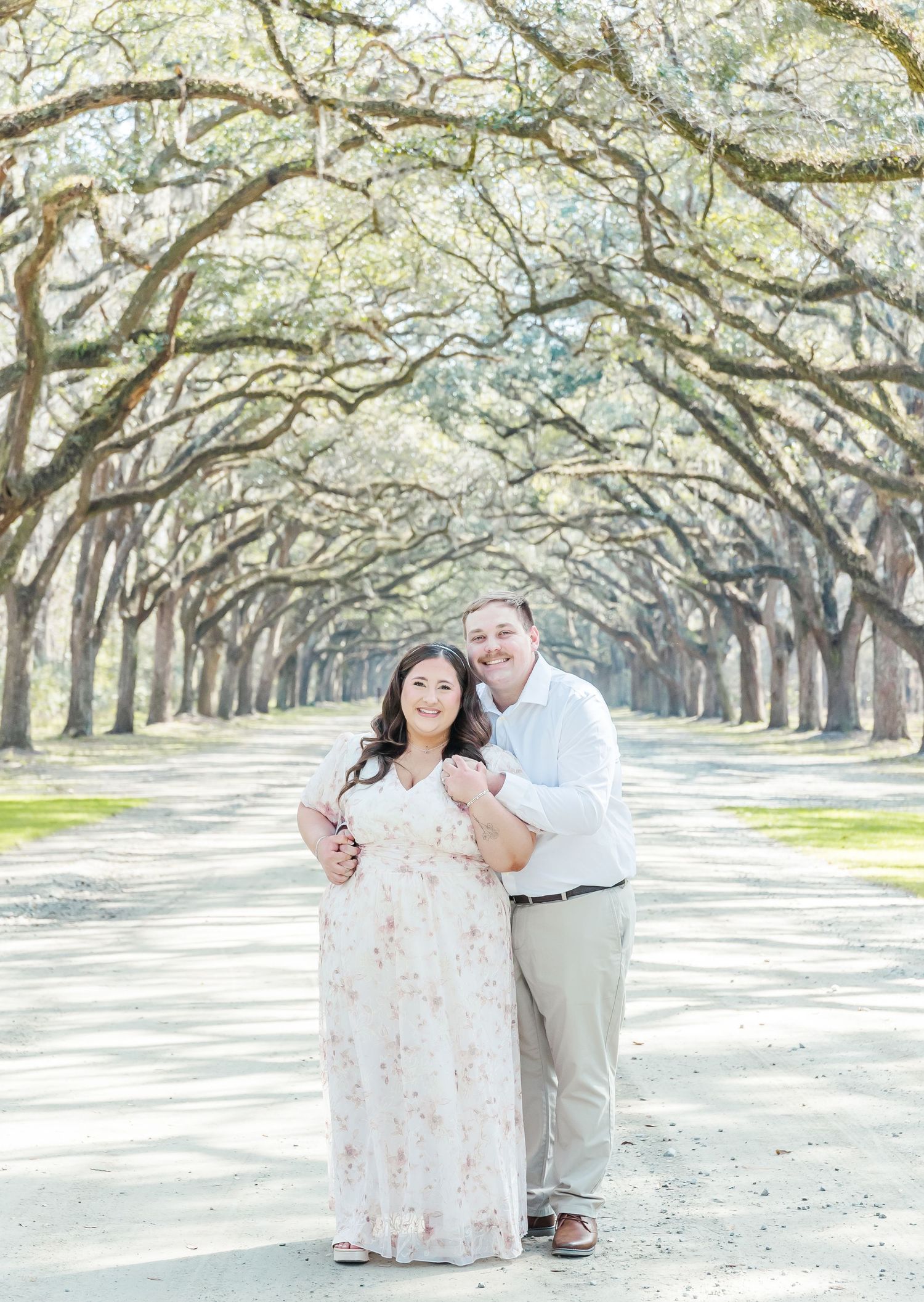 Romantic engagement photo of couple standing on path under oak tree canopy.