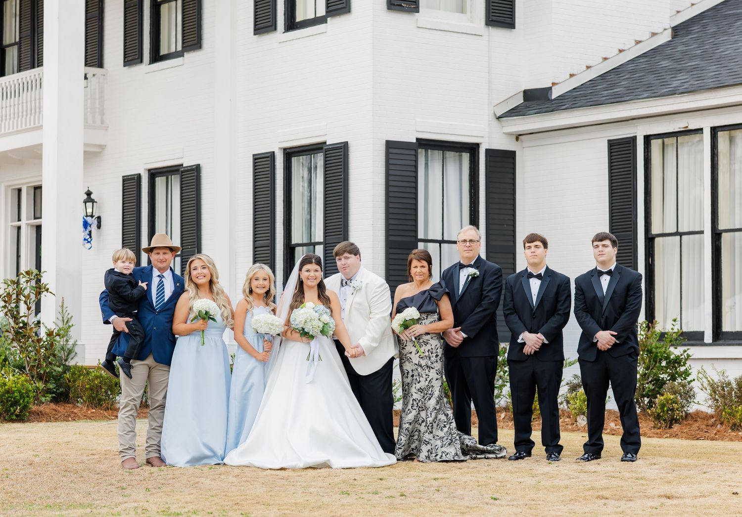 Wedding party poses together outside white estate with bride, groom, family in navy and light blue attire.