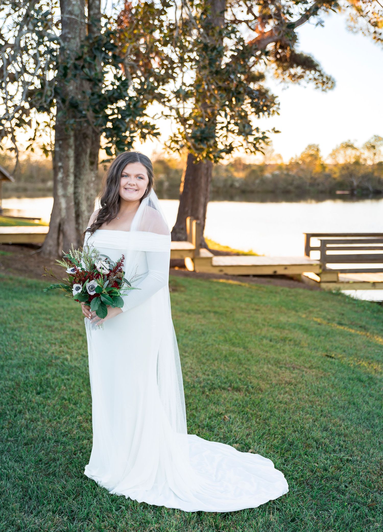 A white wedding gown glows in golden light against a lakeside setting with autumn trees.