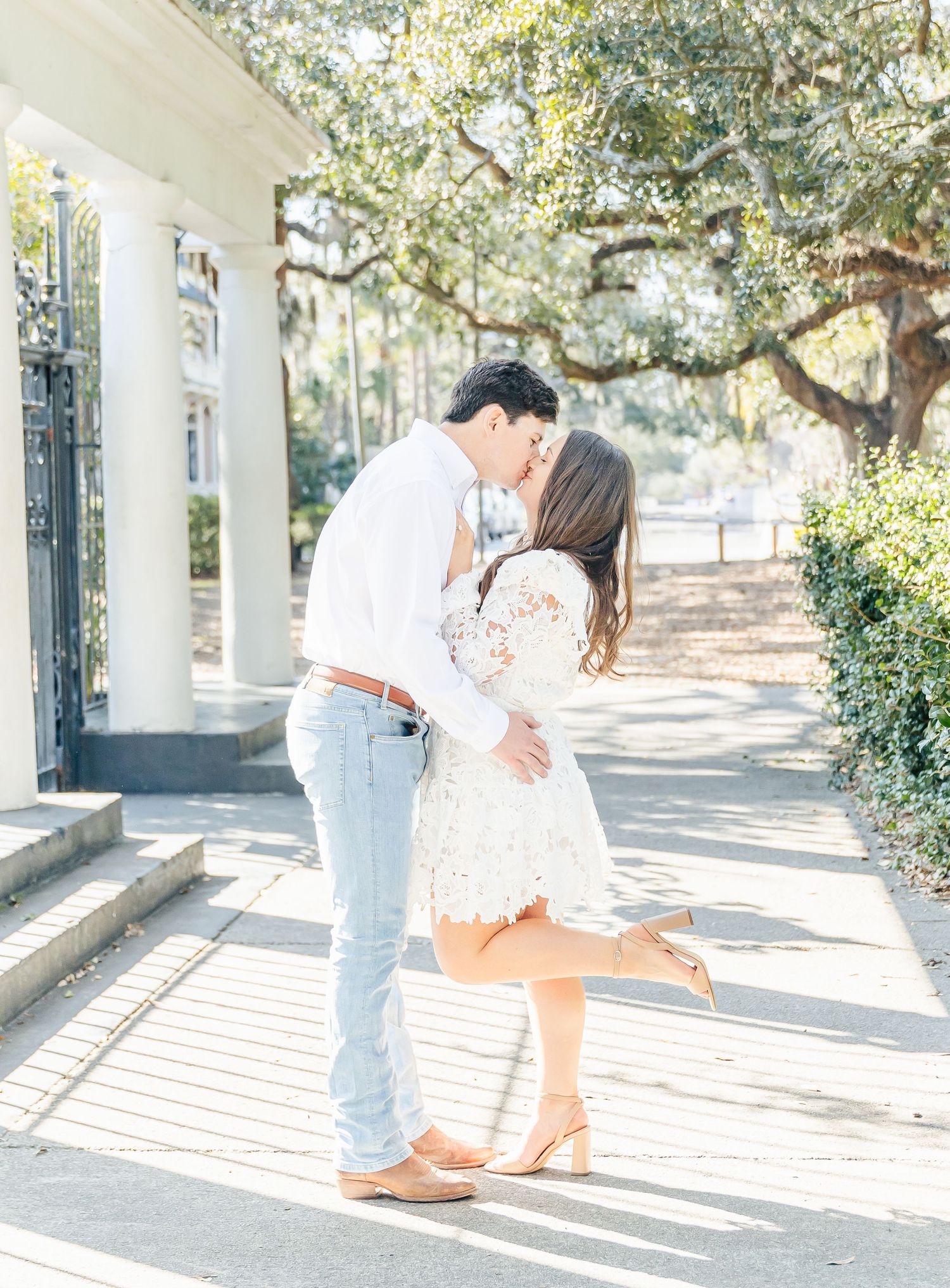 A sweet embrace under white columns and oak trees on a sunny Charleston afternoon.