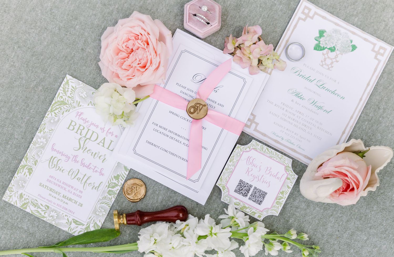 Elegant wedding invitation suite with pink roses, wax seal, and green botanical details on a soft gray background.
