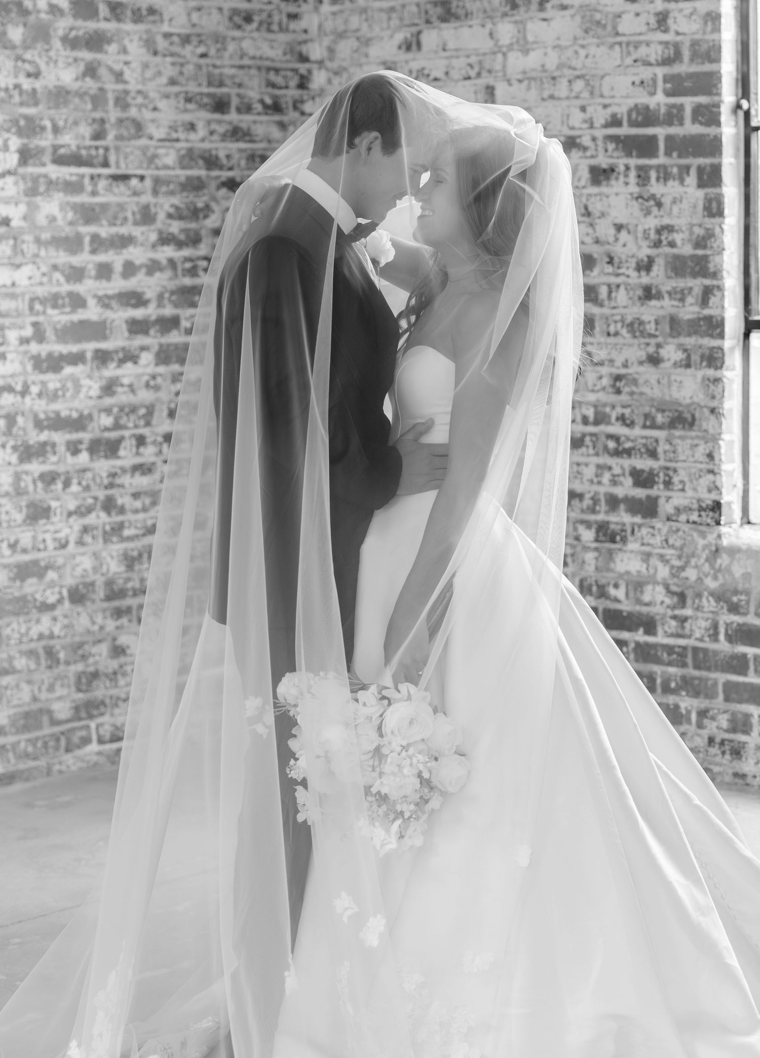 Black and white photo of bride and groom sharing a kiss under the wedding veil.