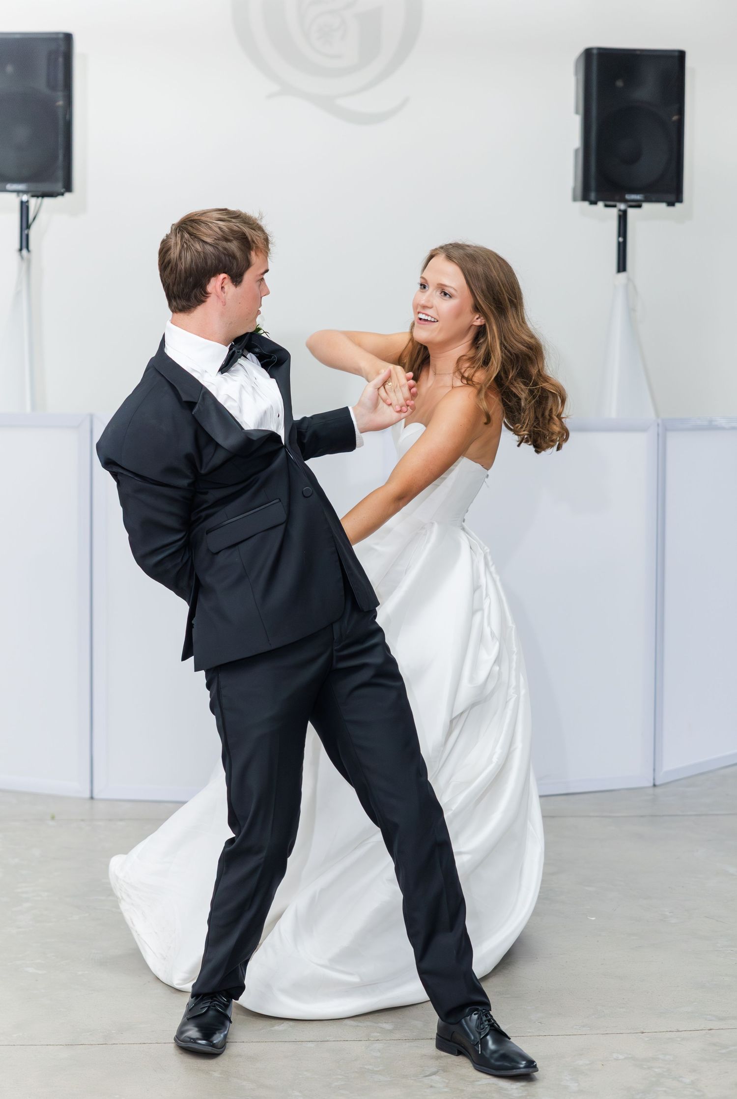 Bride and groom sharing an elegant first dance in a bright white reception hall.