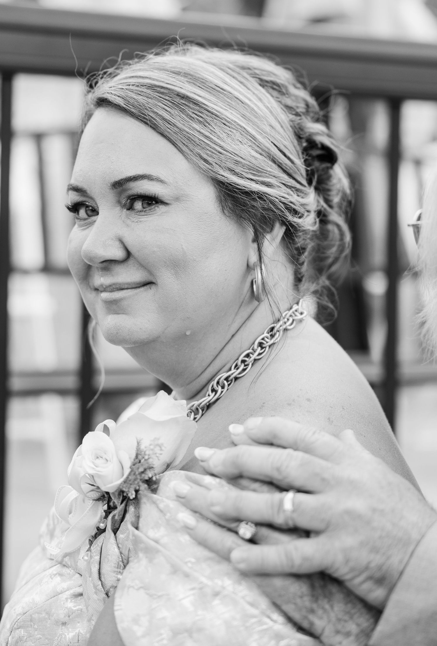 Black and white portrait of smiling woman with updo wearing floral corsage at wedding celebration.