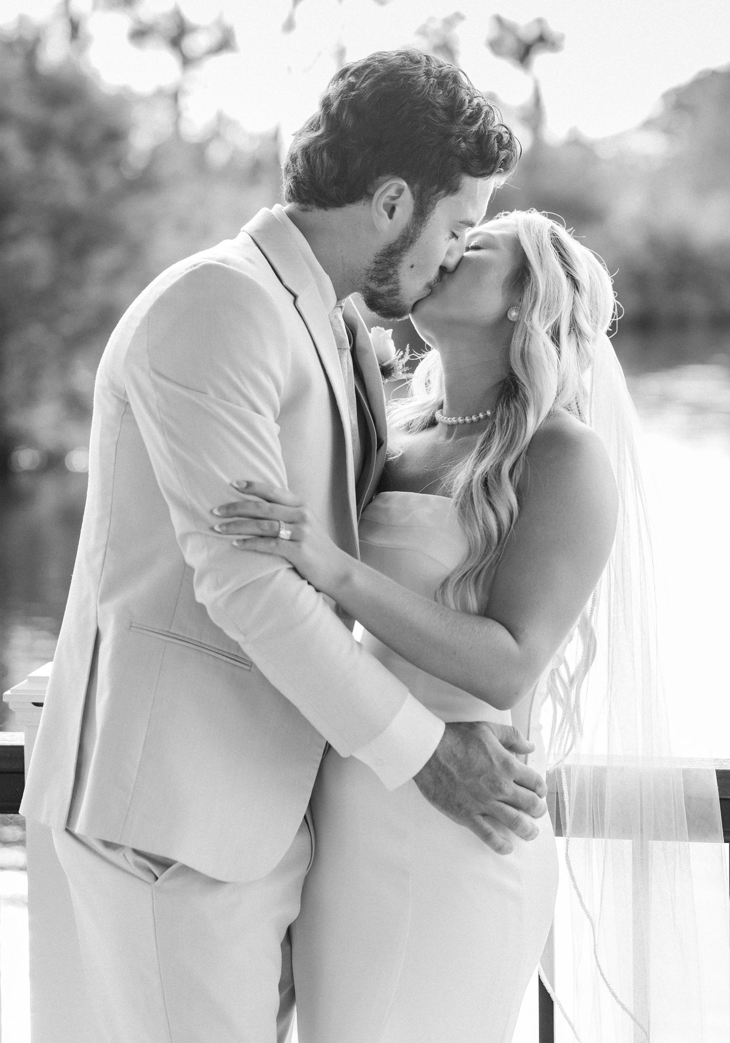 Black and white photo of bride and groom sharing a romantic kiss outdoors on their wedding day.