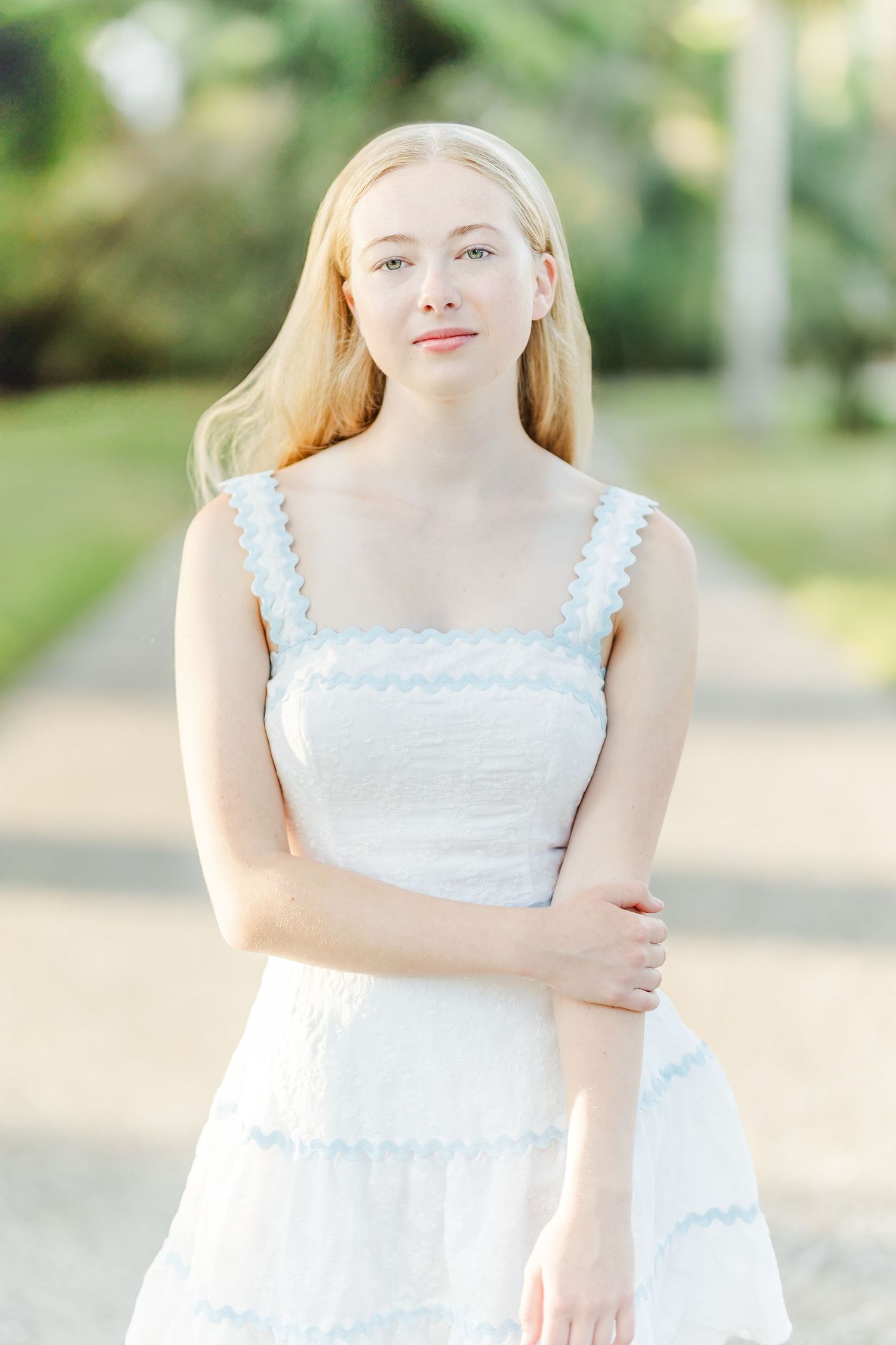 A person in a white sleeveless summer dress stands outside in a sunny garden setting.