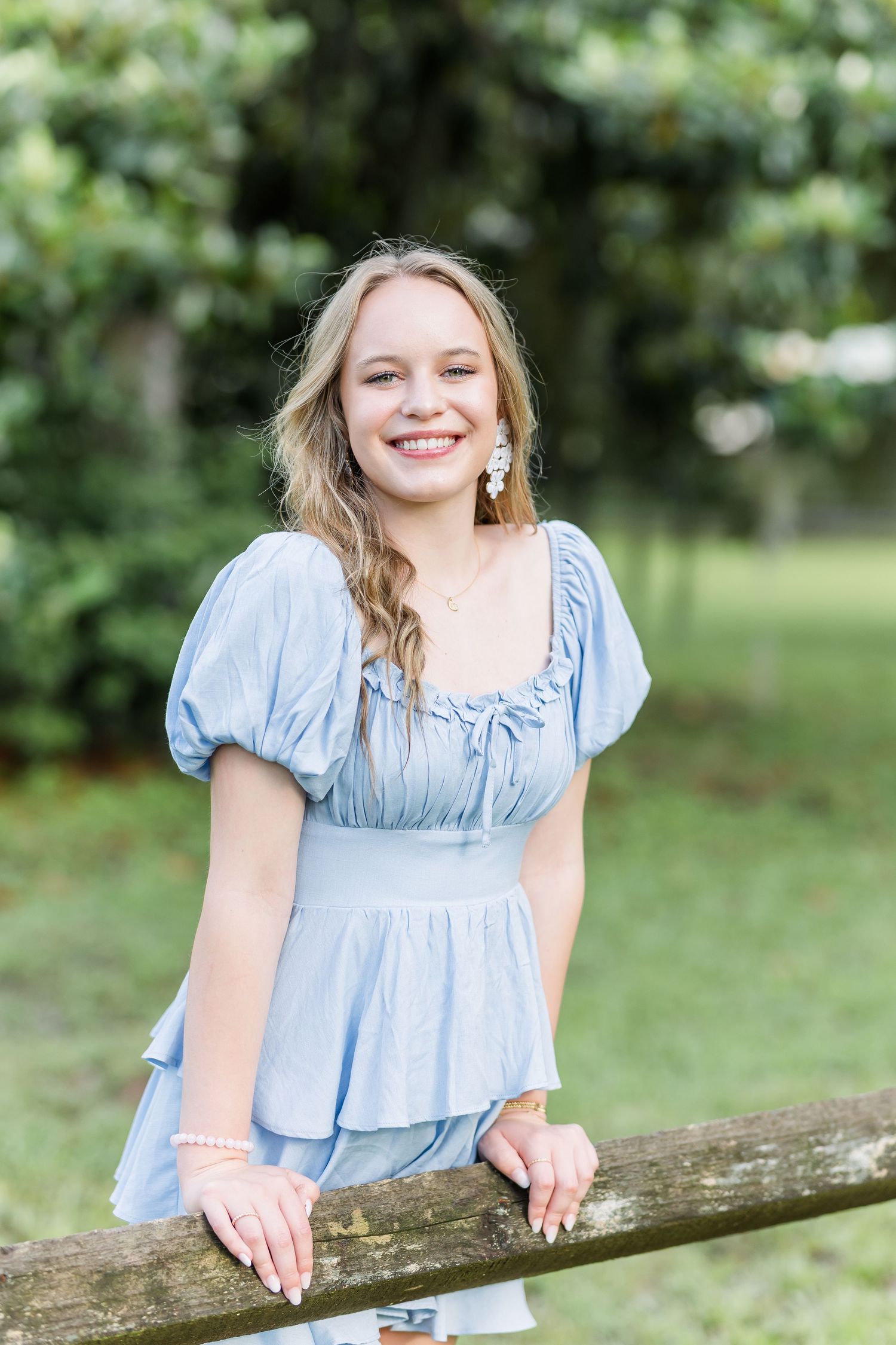 Playful poses against a rustic wooden fence in a light blue ruffle dress.