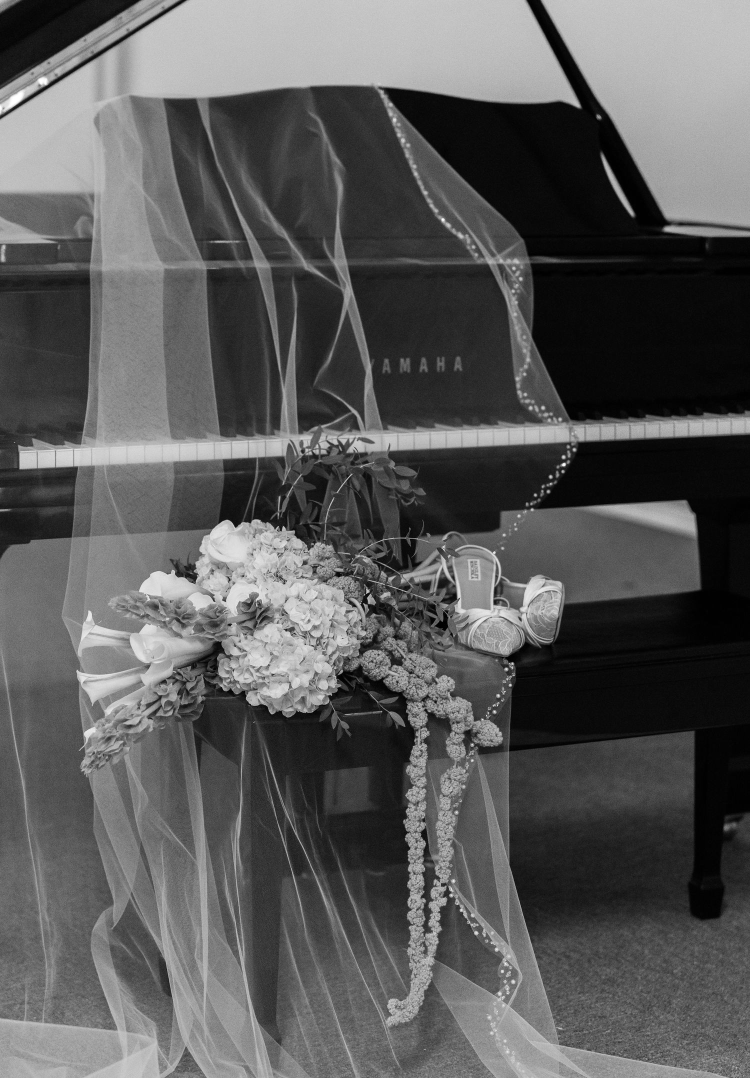 Black and white photo of bridal veil and bouquet draped over Yamaha grand piano bench.