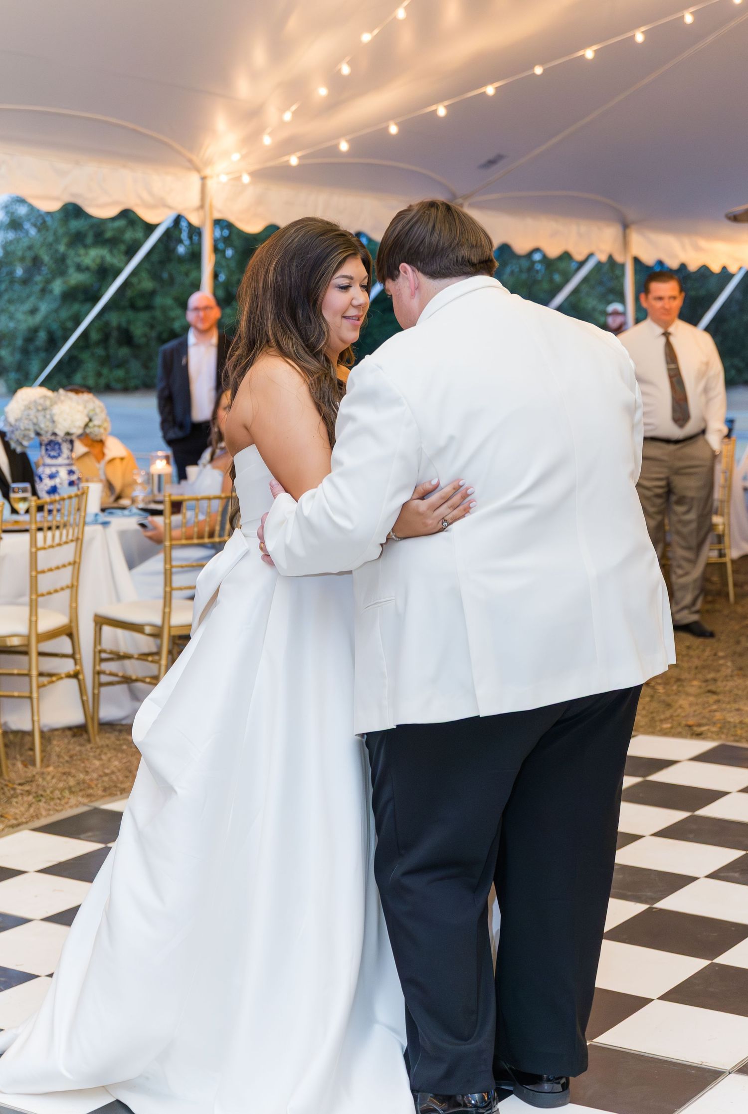 Bride and groom share first dance under a tent with string lights at outdoor wedding reception.