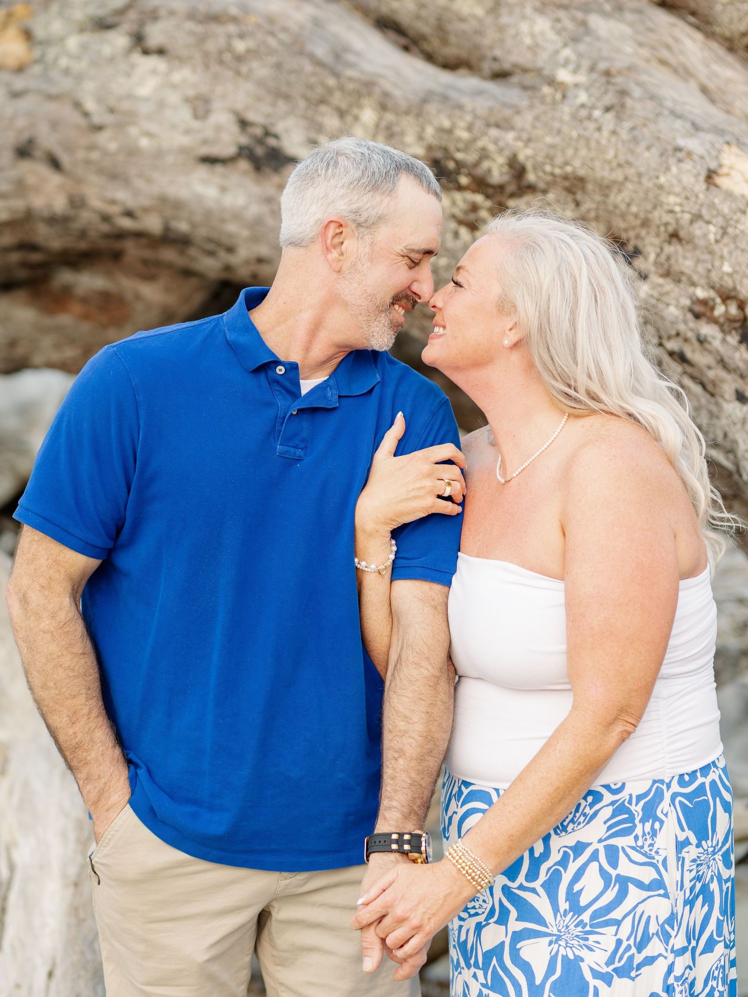 Senior couple shares an intimate moment together against a rocky background wearing blue and white summer attire.