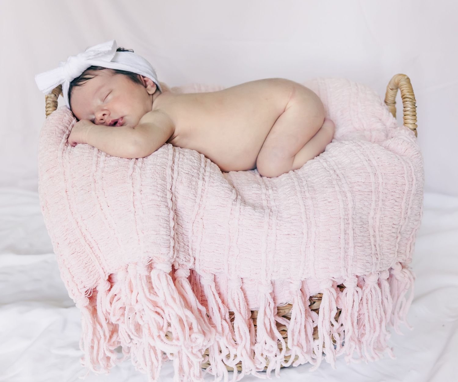 Peaceful newborn sleeps on pink fringed blanket in basket.