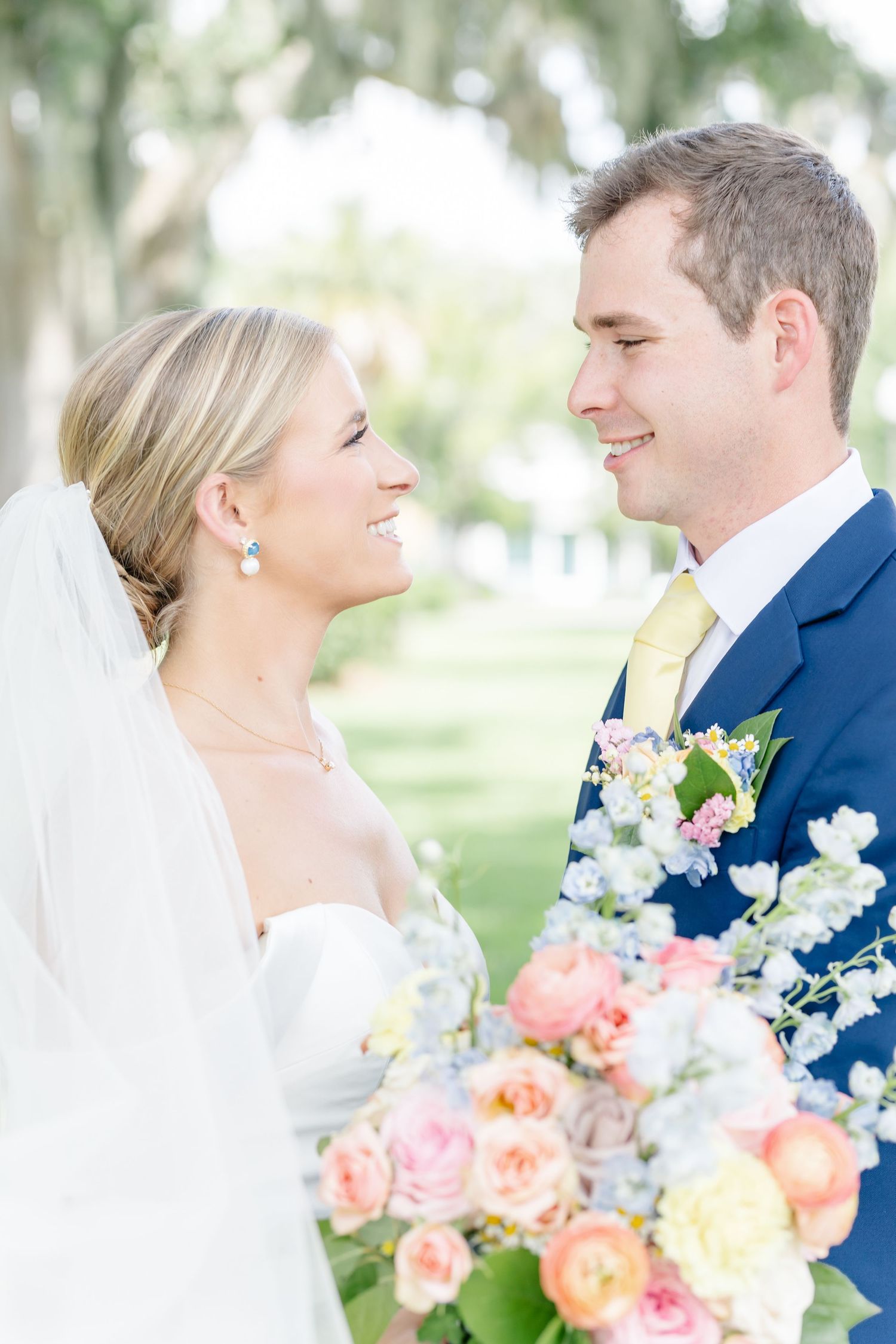 A bride and groom share joyful moments together while holding a beautiful coral and white floral bouquet.