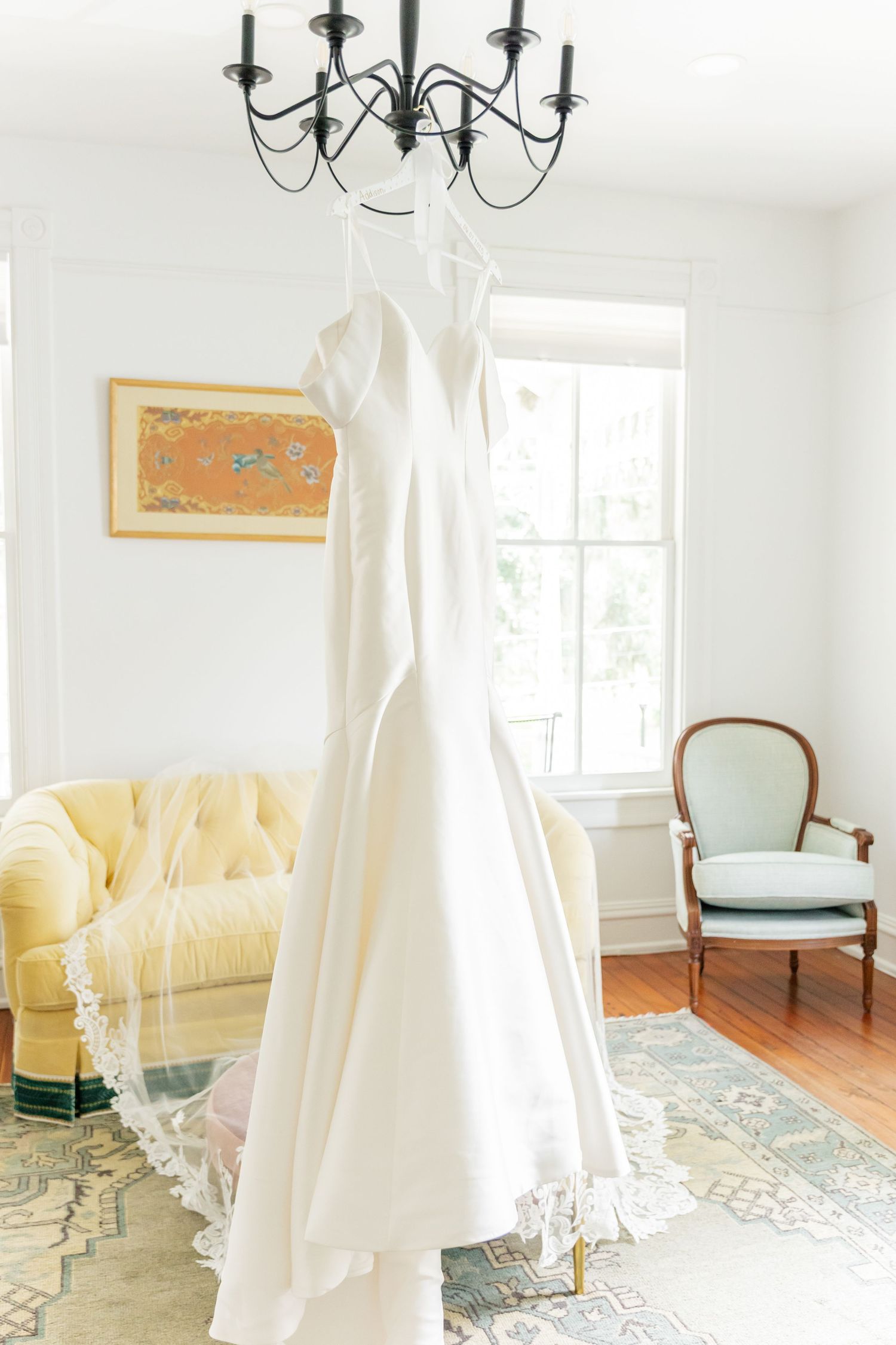 Elegant white studio space with yellow vintage sofa, chandelier, and flowing white curtains creating a romantic atmosphere.