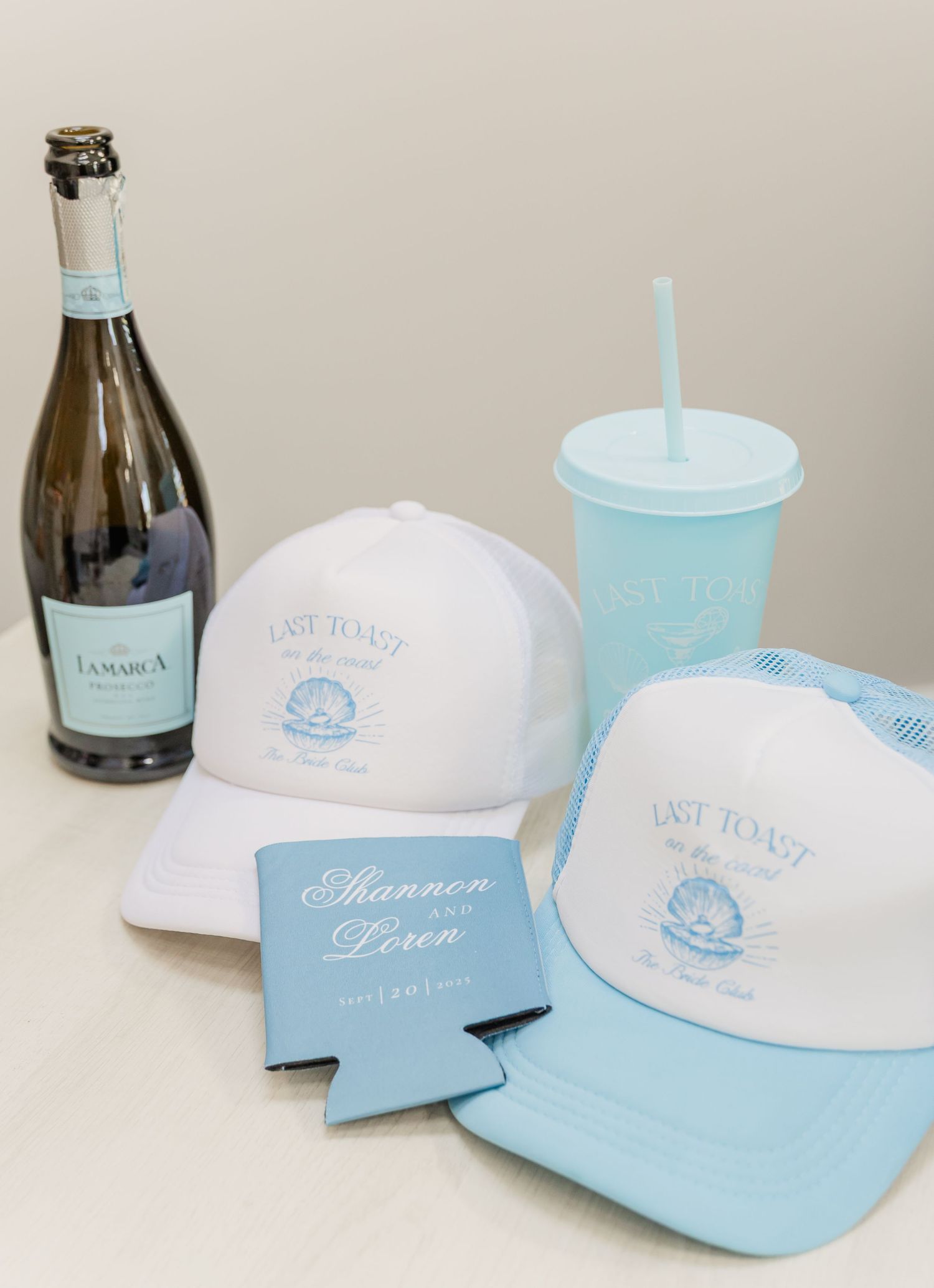 Light blue and white beach-themed merchandise including baseball caps, drink koozies, and a bottle displayed together.