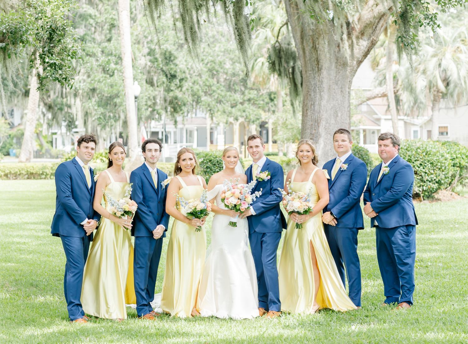 Wedding party in navy suits and yellow dresses posed under Spanish moss trees.