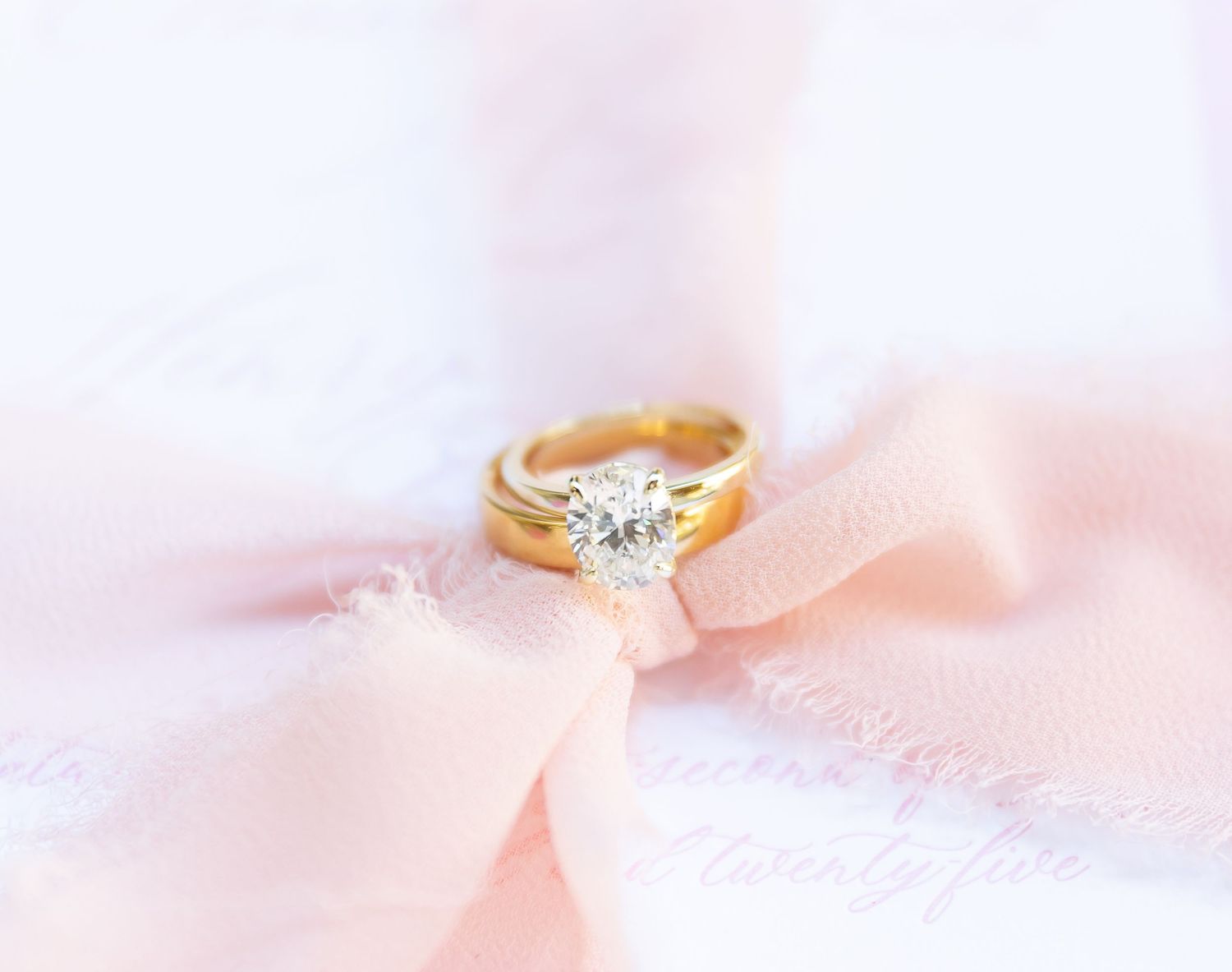 An elegant diamond engagement ring sparkles against soft pink fabric creating a romantic atmosphere.
