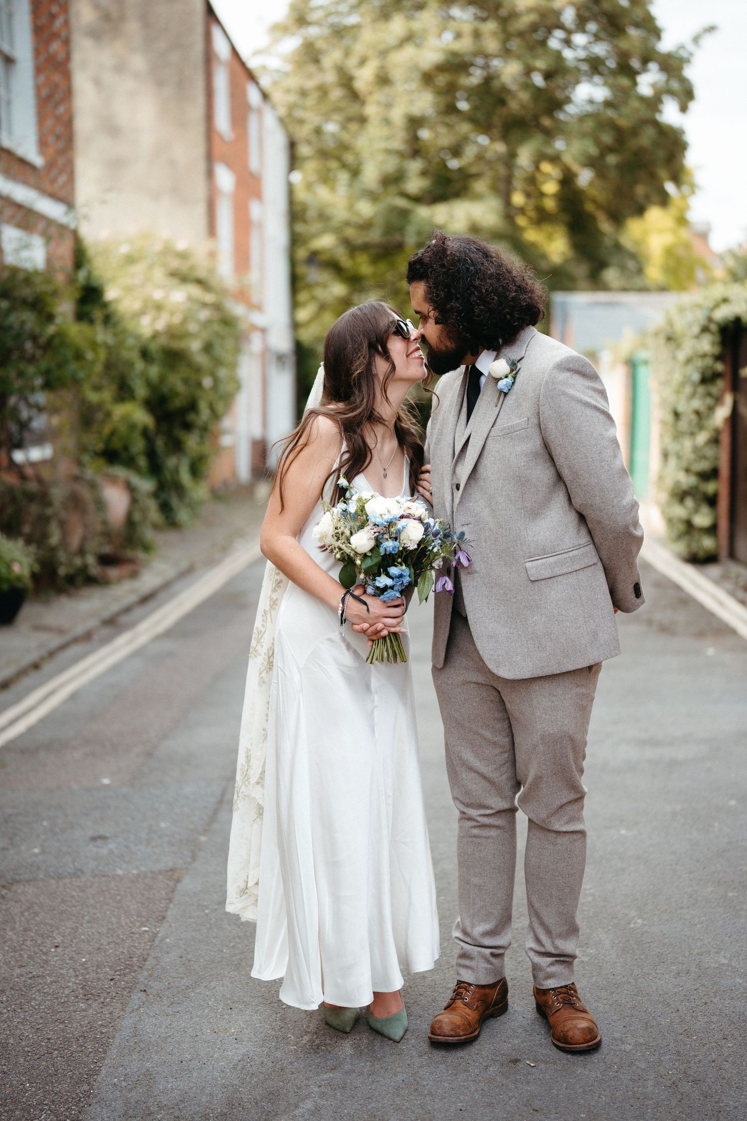 A couple shares an intimate moment on their wedding day, with the bride holding a beautiful bouquet on a quaint street.