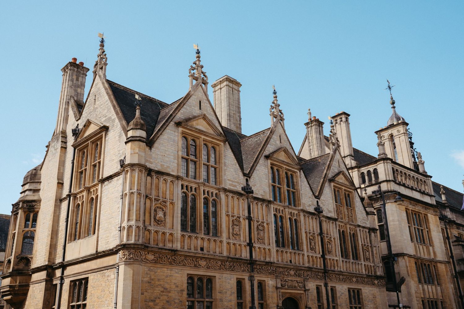 Historic Gothic Revival architecture with ornate stone façade and pointed gables at Oxford University against blue sky.