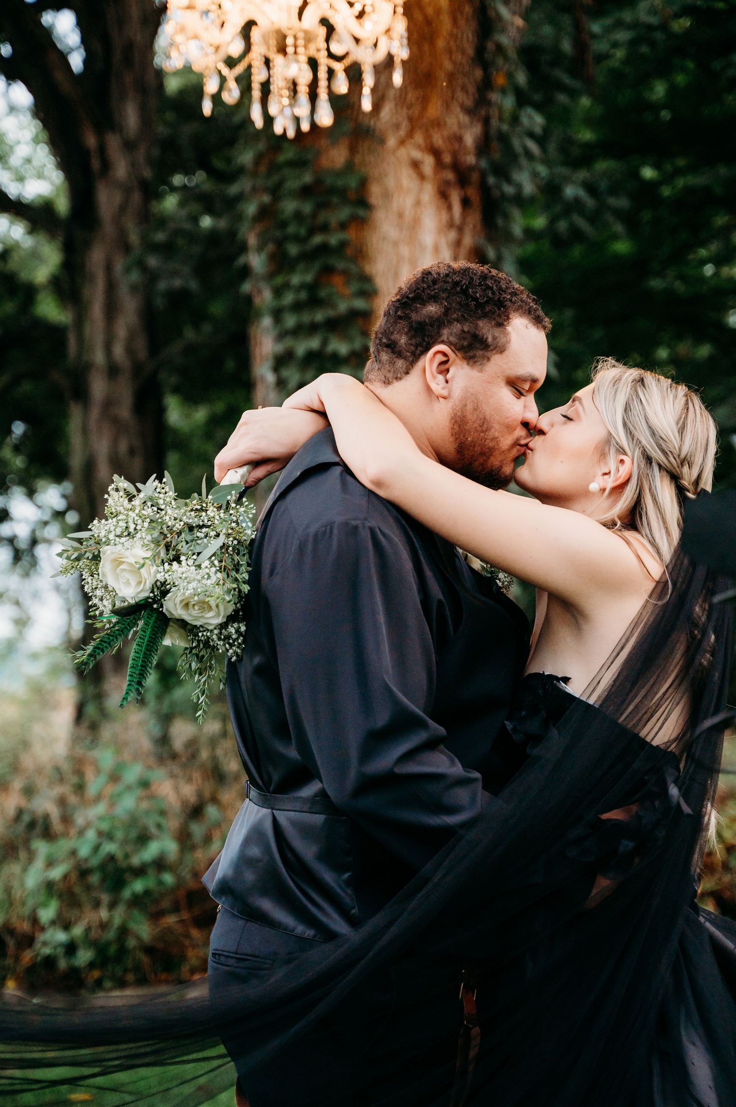 A romantic moment captured under a crystal chandelier in a garden setting with a white bouquet.