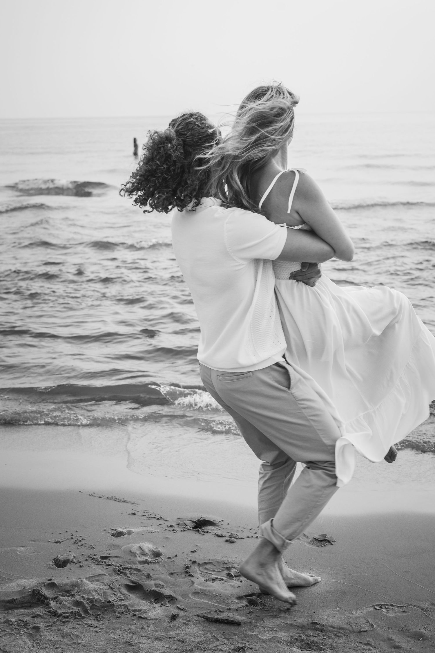 A romantic black and white photo of a couple embracing and dancing by the ocean shore.