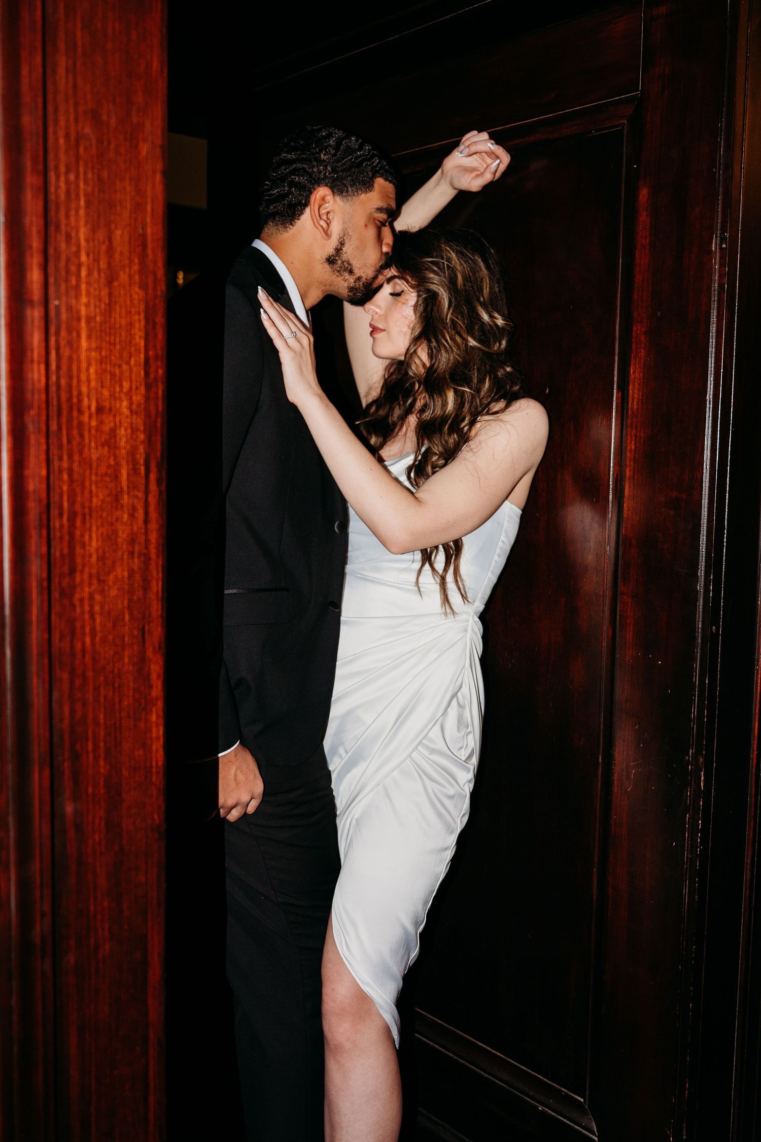A couple shares an intimate dance moment in an elegant wood-paneled room.