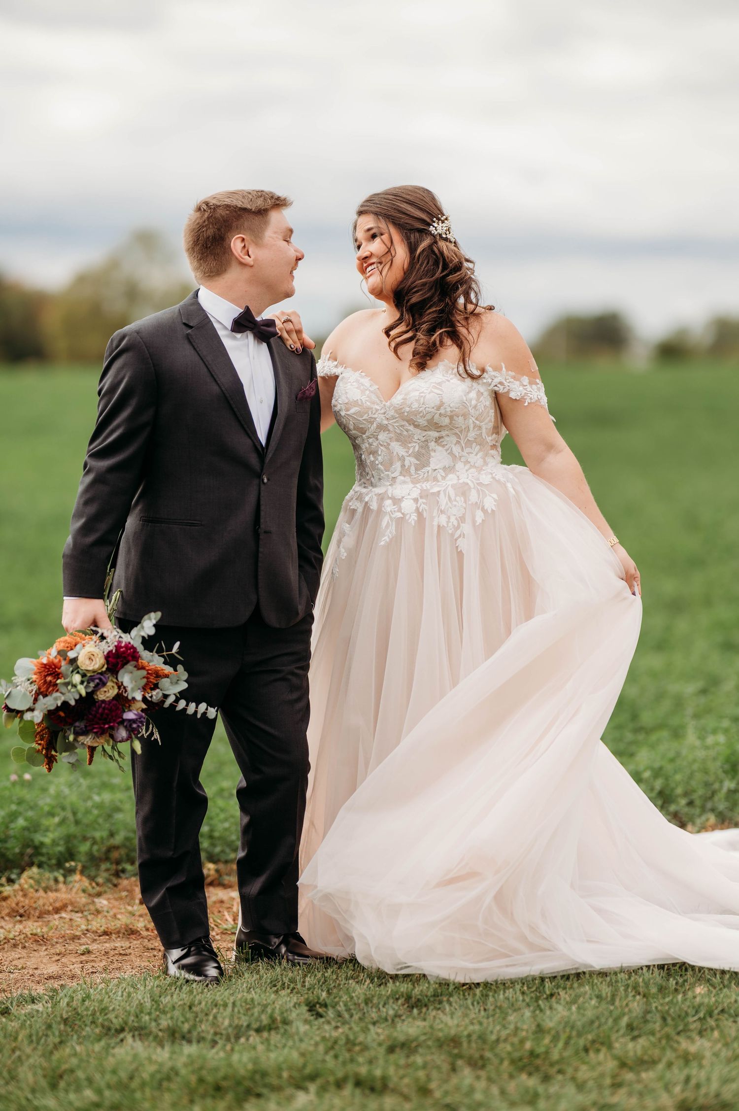 A couple poses together in a grassy field during their wedding photoshoot.
