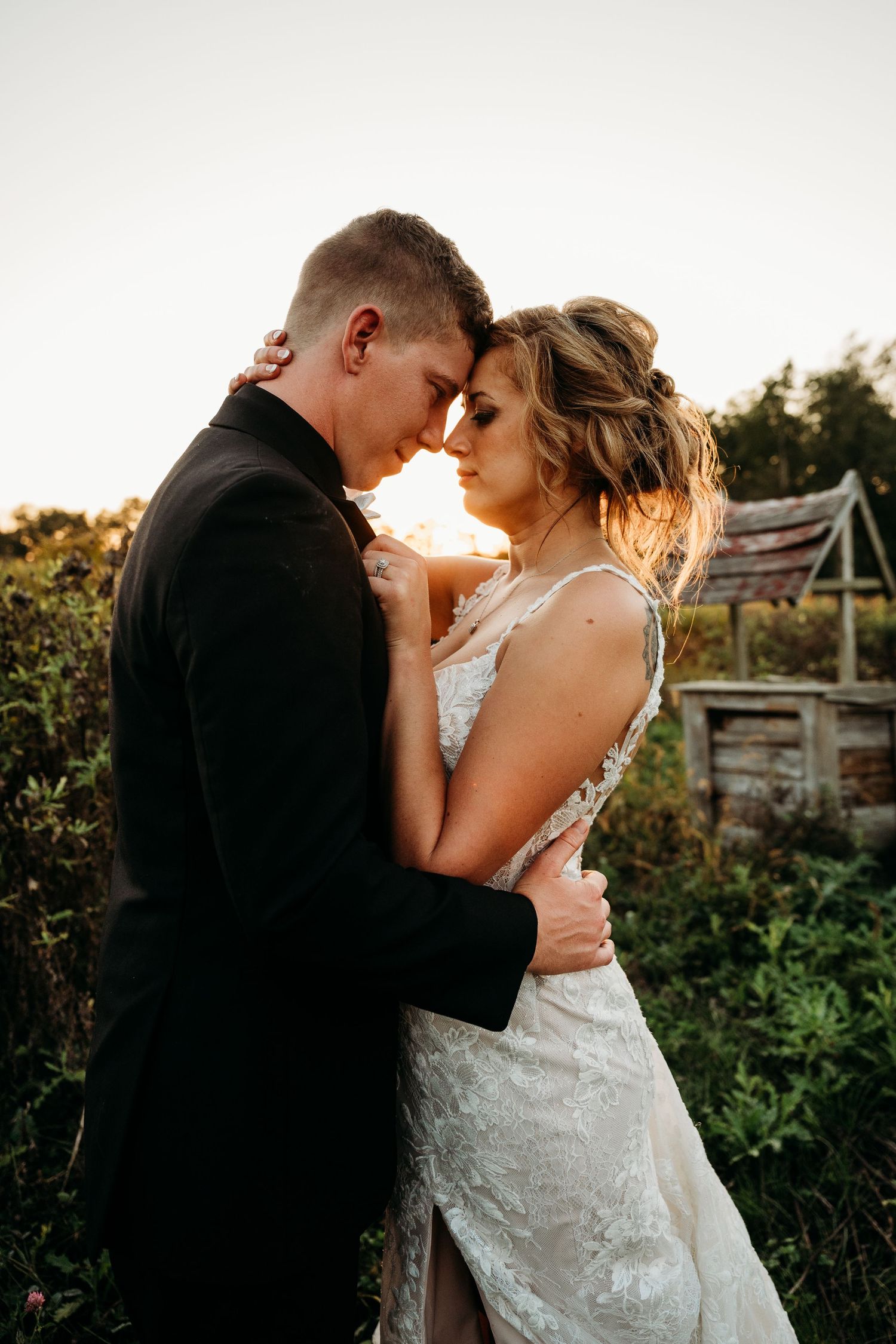 A romantic wedding couple embraces at sunset in a garden setting with warm golden light.