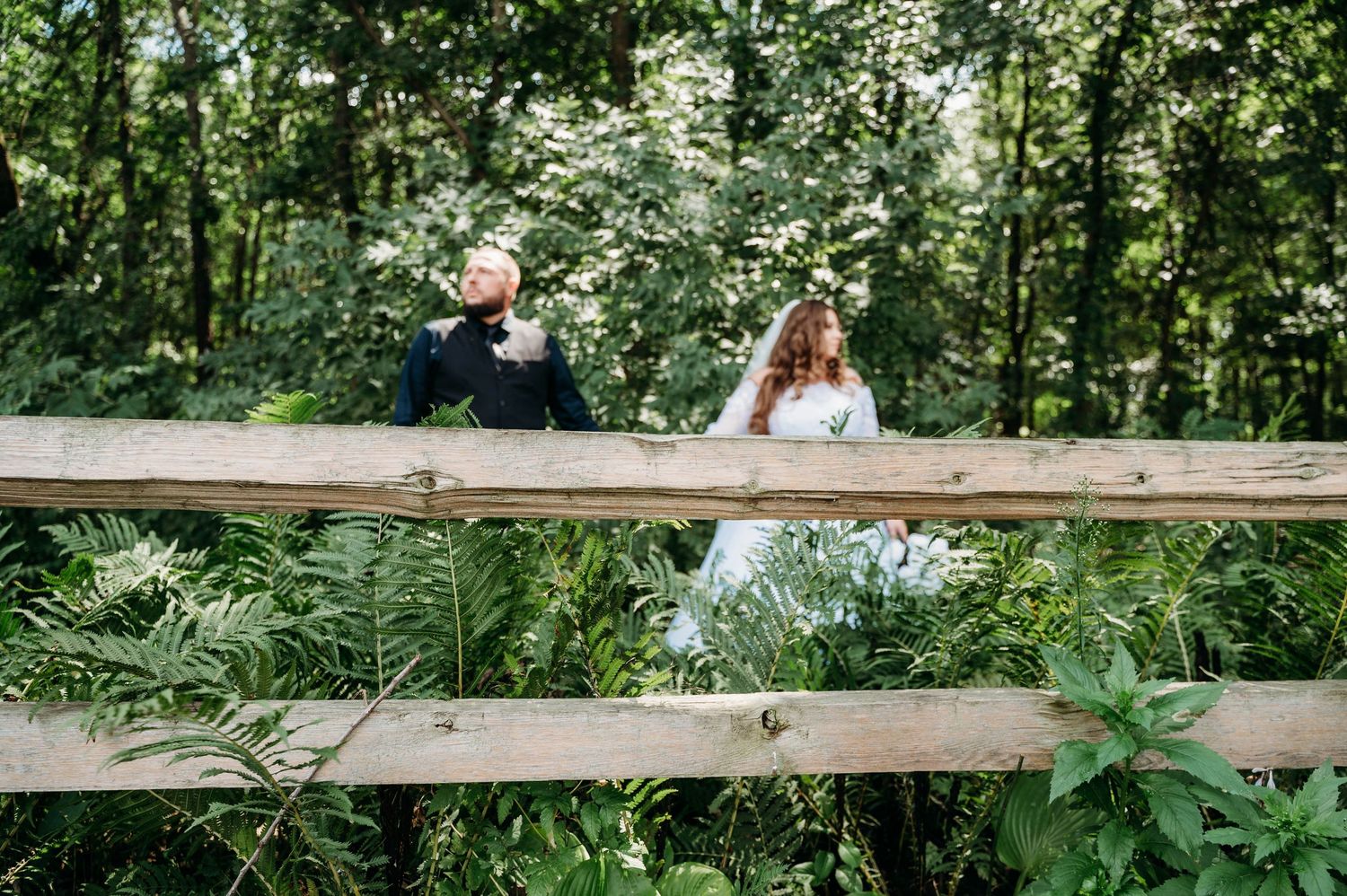 A couple sits together on a wooden bench surrounded by lush green foliage in a peaceful outdoor setting.