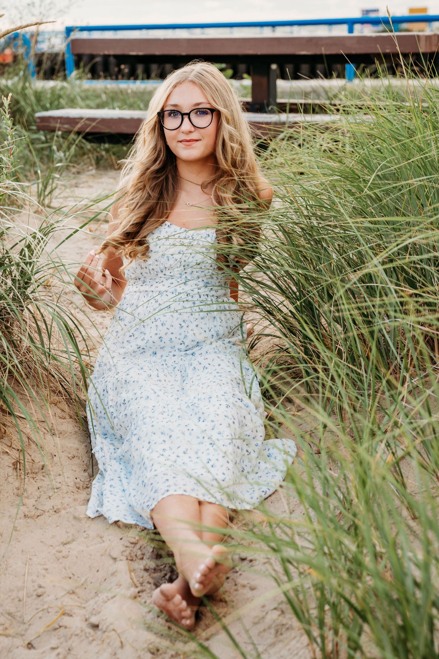 A charming beach photoshoot scene with a white dress and tall grasses along the sandy shore.