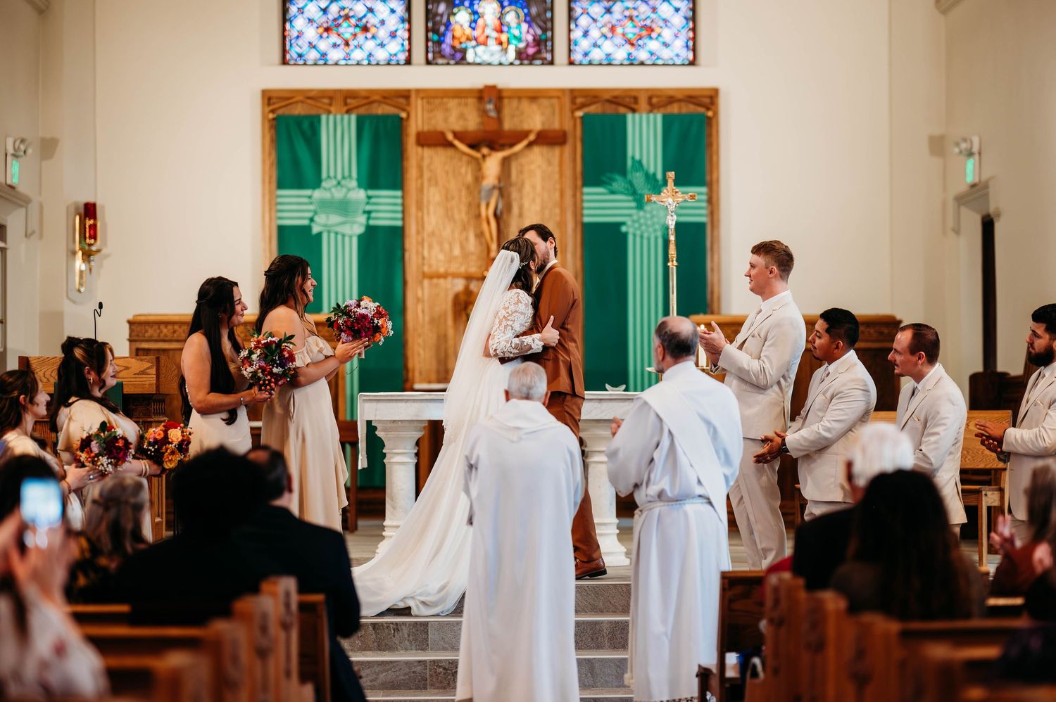 A wedding ceremony in progress inside a traditional church with stained glass windows and green doors.