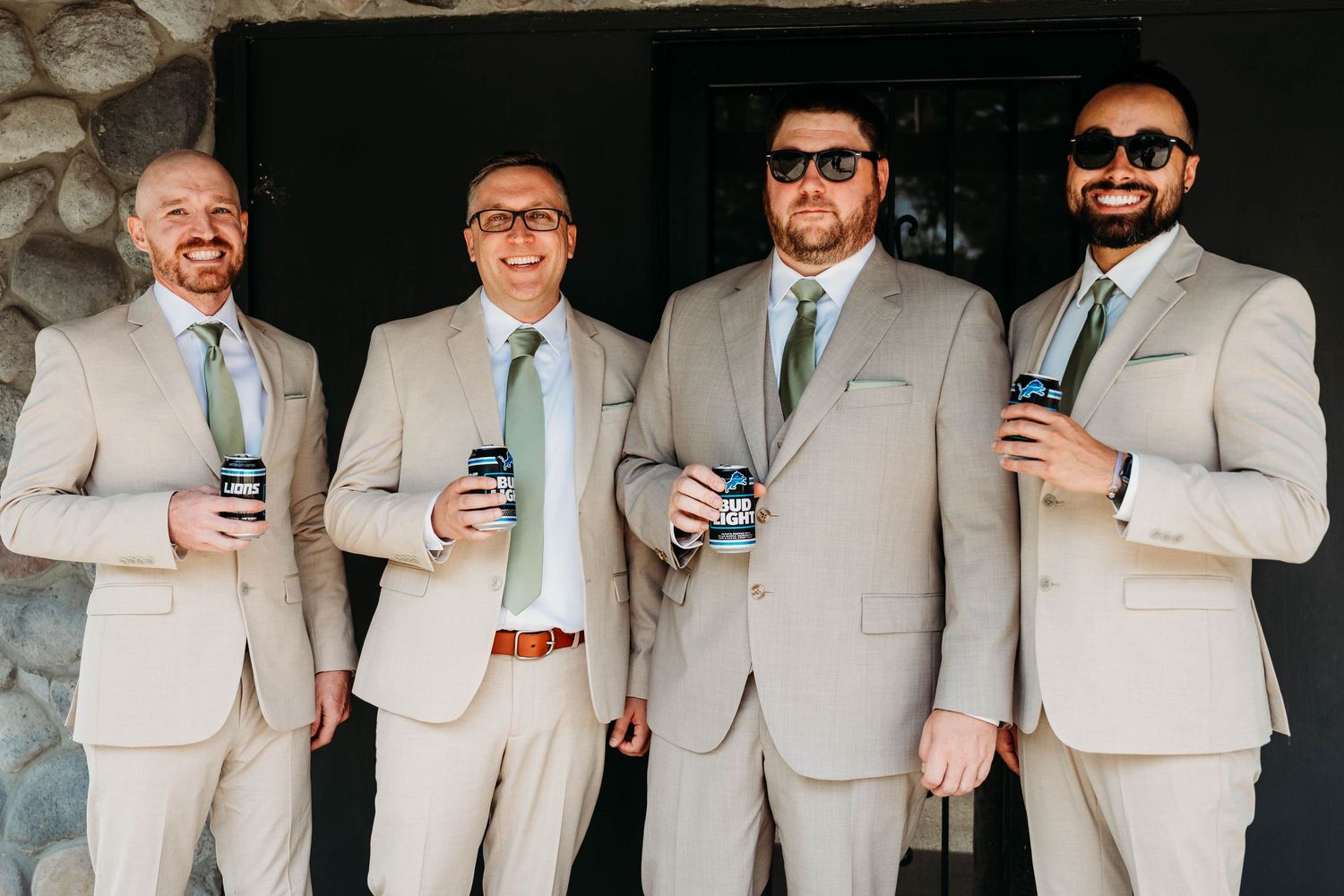 A series of groomsmen in light gray suits posing together while holding drinks at a wedding celebration.