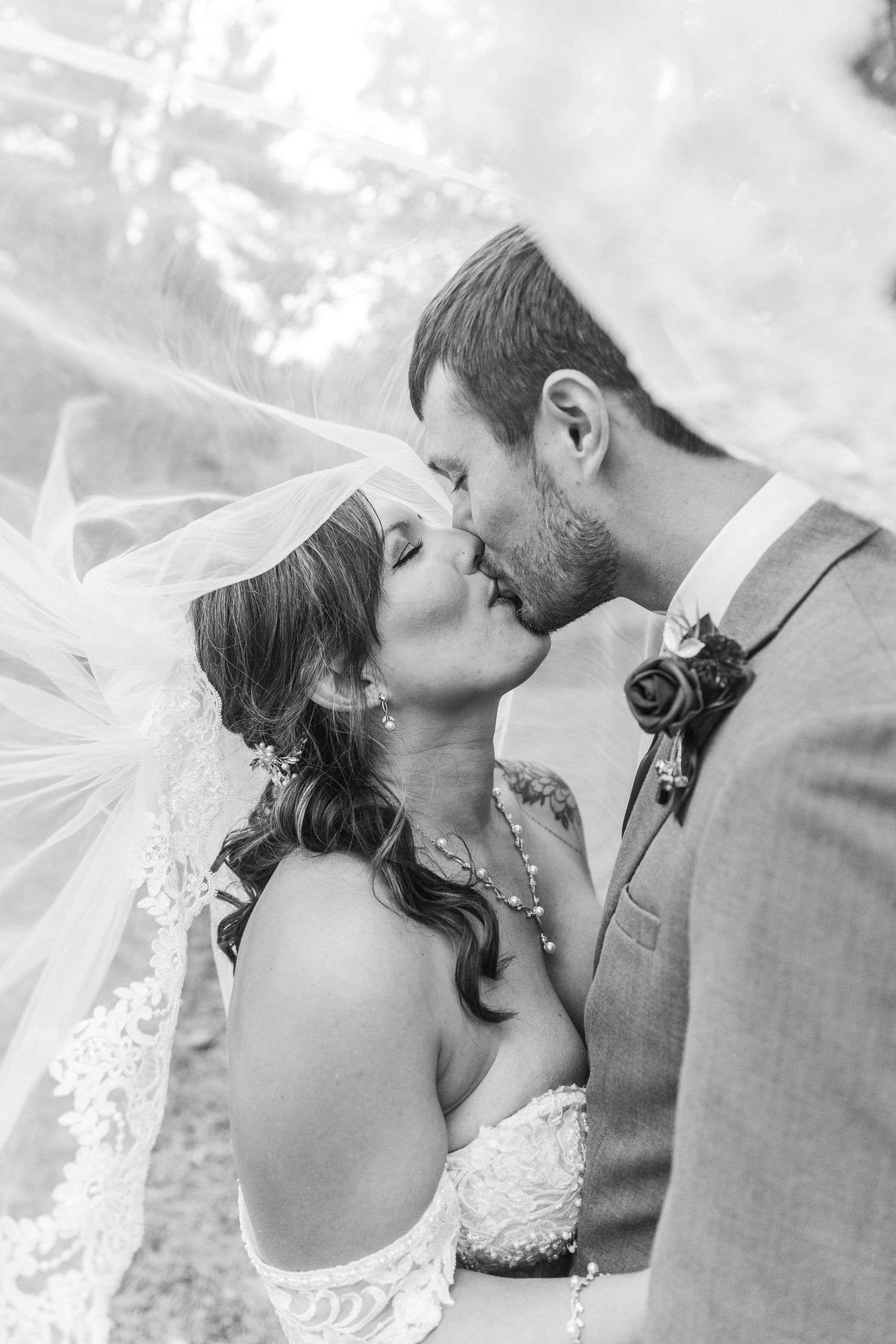 Black and white wedding photo of bride and groom sharing a romantic kiss under a flowing veil.
