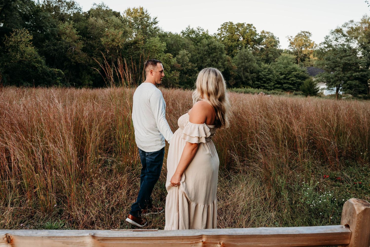 Romantic couple embraces in a rustic field of tall brown grass during golden hour.