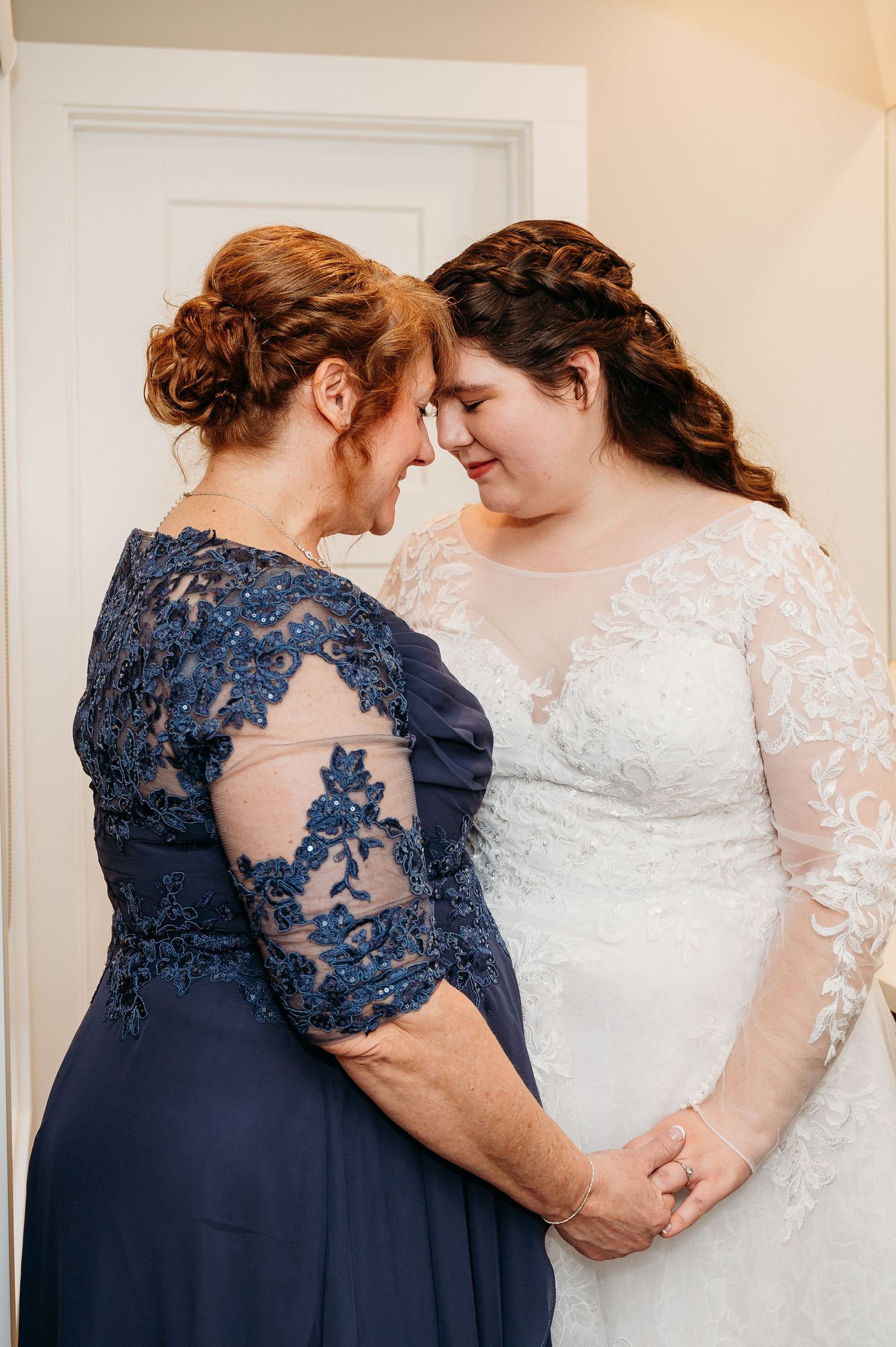 A tender moment shared between two women wearing elegant blue and white lace dresses with braided hairstyles.
