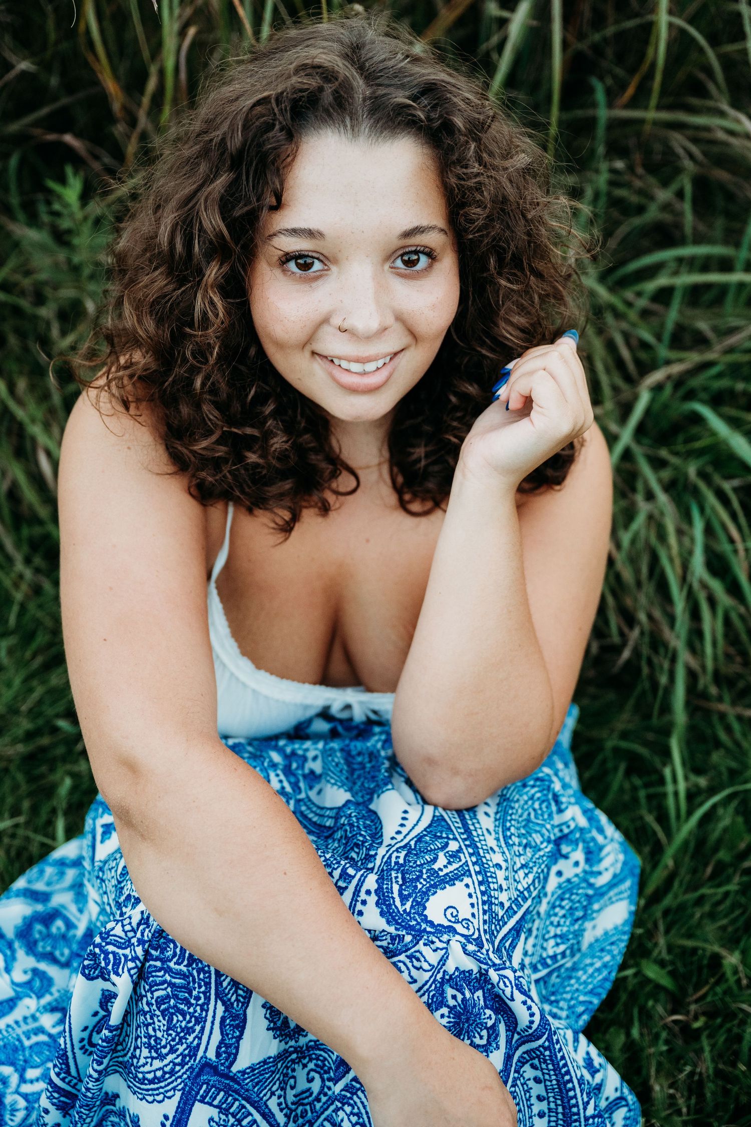 Outdoor portrait in blue patterned dress sitting against natural green foliage background.