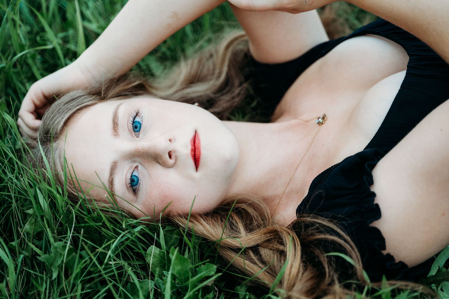 A portrait series of a person lying in green grass wearing a black top and showing different expressions and poses.