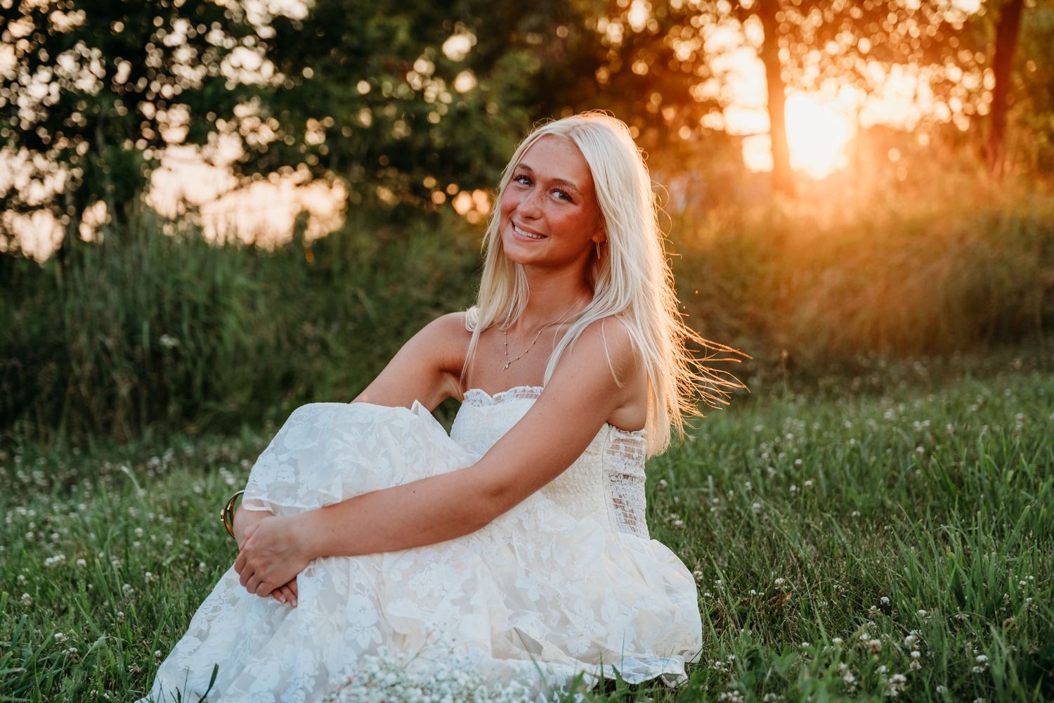 A bride in a white dress poses in a grassy field during golden hour sunset.